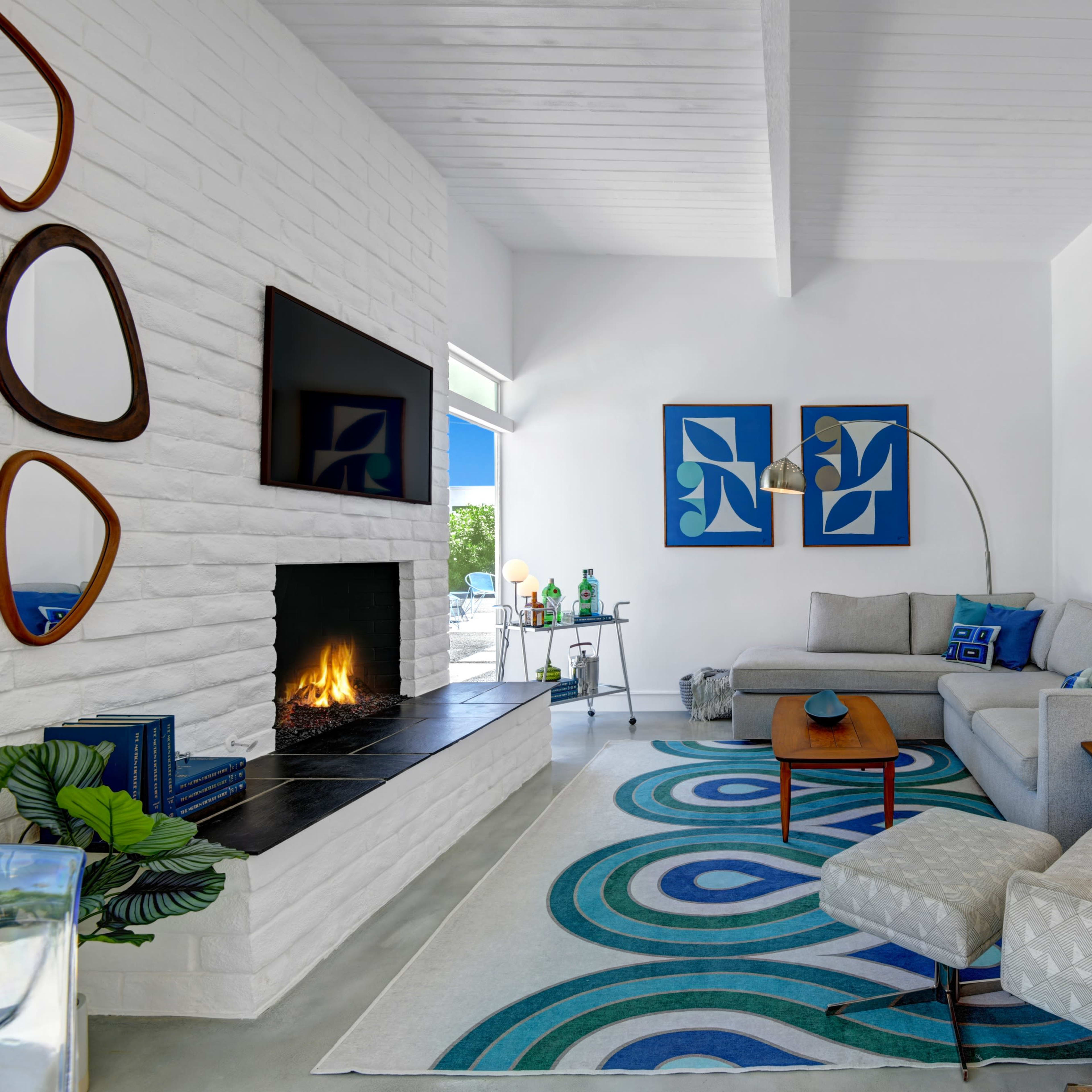 A modern living room with a white brick fireplace, a gray sofa, and colorful abstract artwork on the walls.