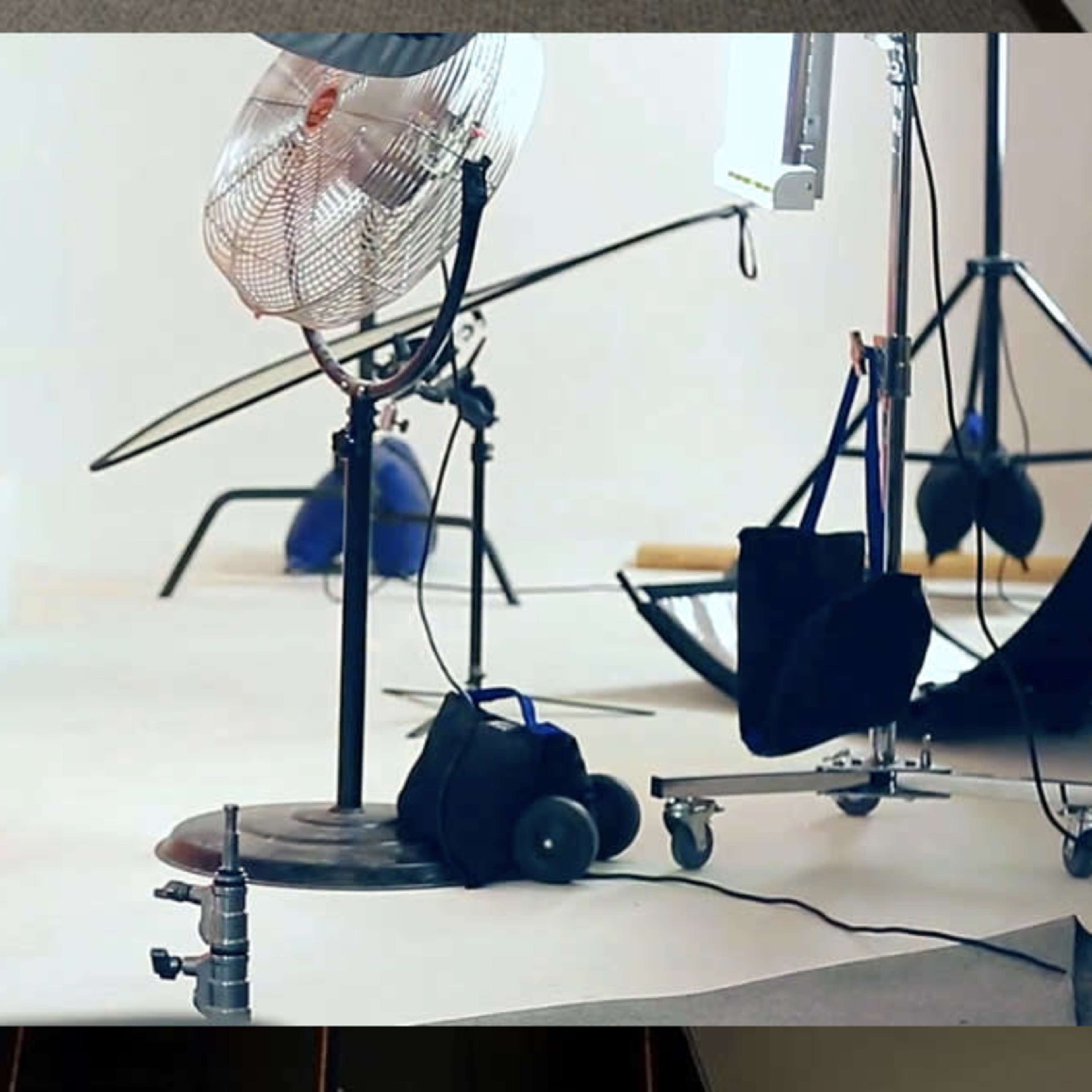 A photography studio setup featuring a fan, various lighting equipment, and backdrops on a white floor.