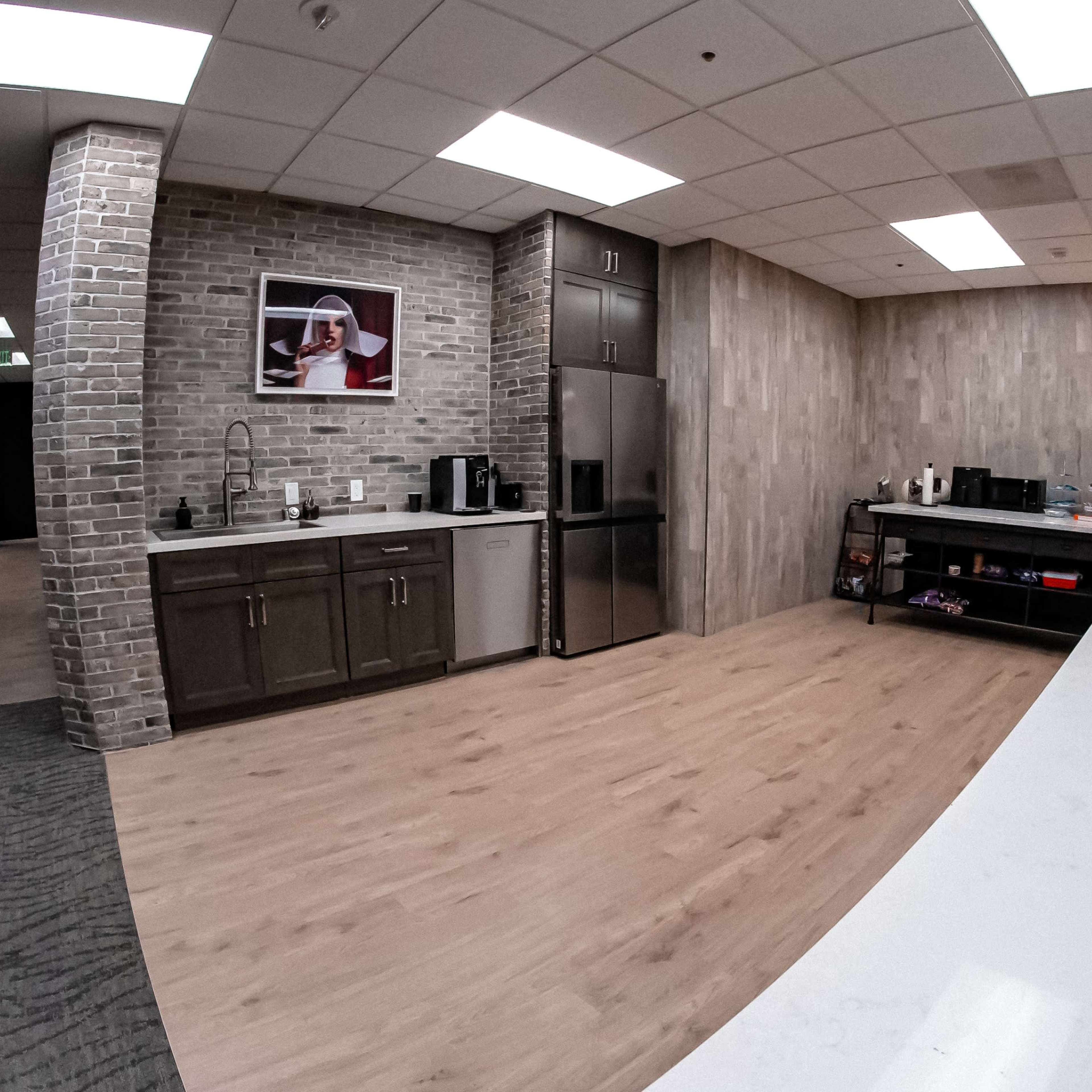 A modern office kitchen area featuring a sleek countertop, appliances, and a brick wall backdrop.