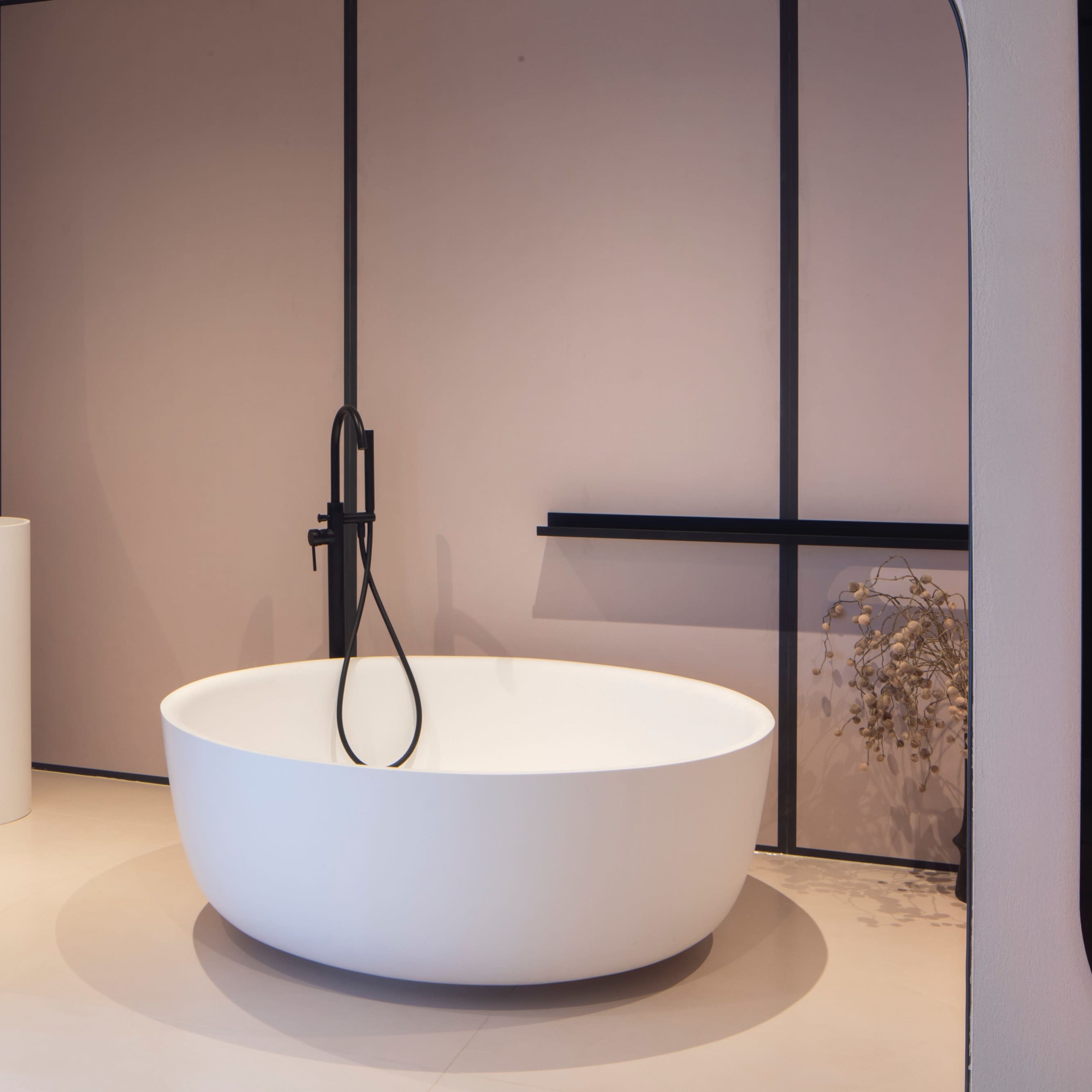 A modern bathroom with a freestanding white bathtub, a minimalist sink, and a large mirror against a pink wall.