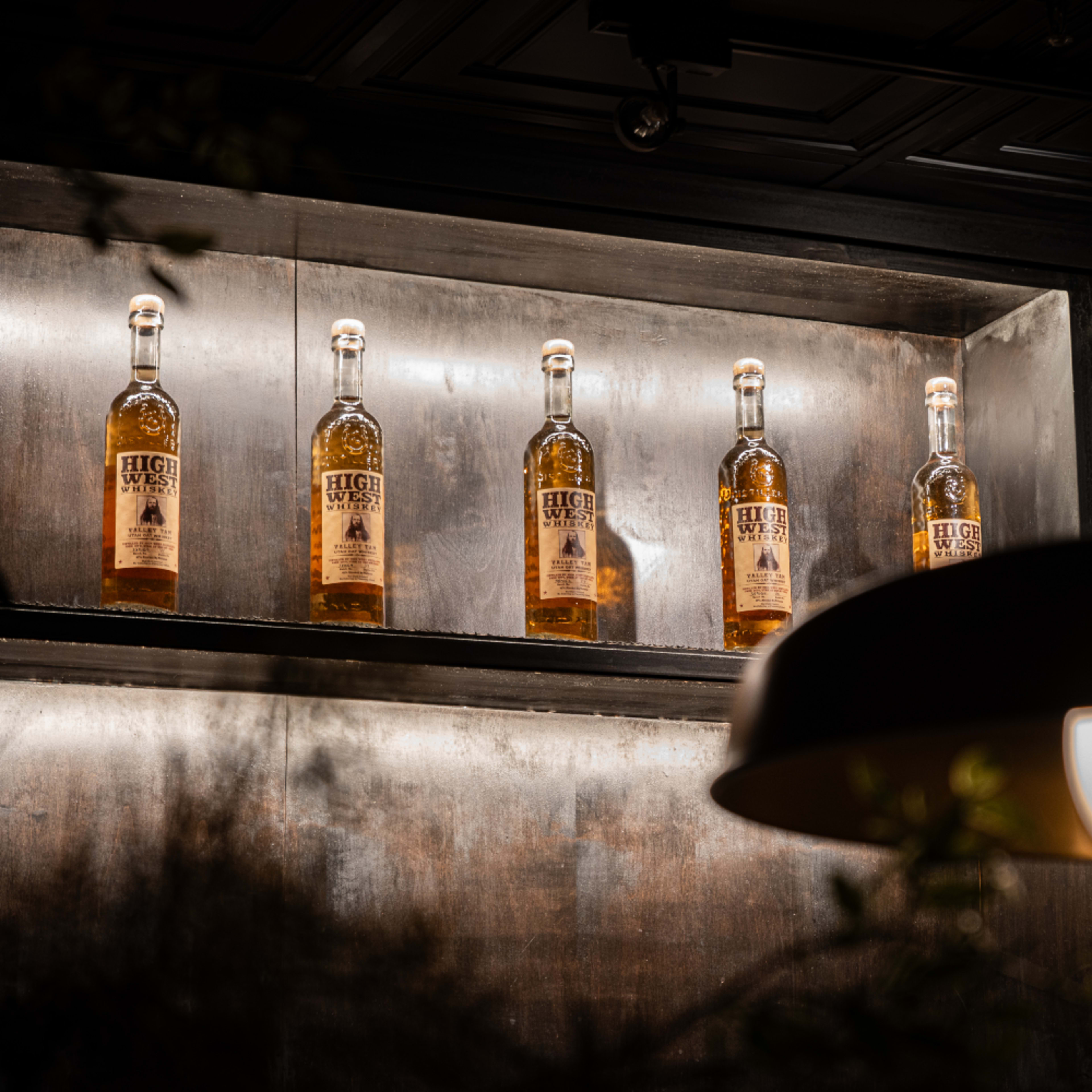 A row of bottles labeled "HUGE" is displayed on a wooden shelf with a pendant light in the foreground.