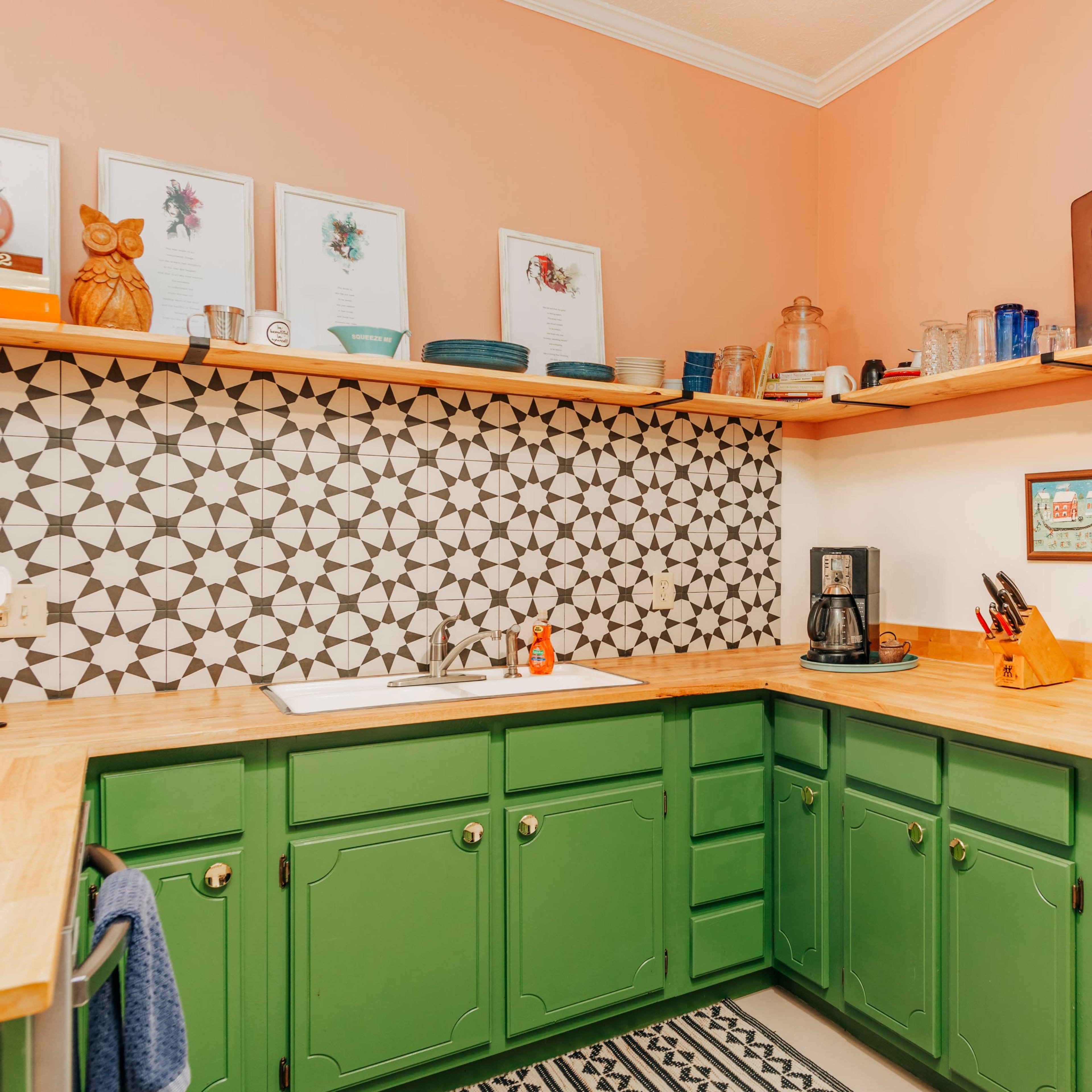 A kitchen with green cabinets, a patterned tile backsplash, and wooden countertops, featuring an array of kitchen utensils and appliances.