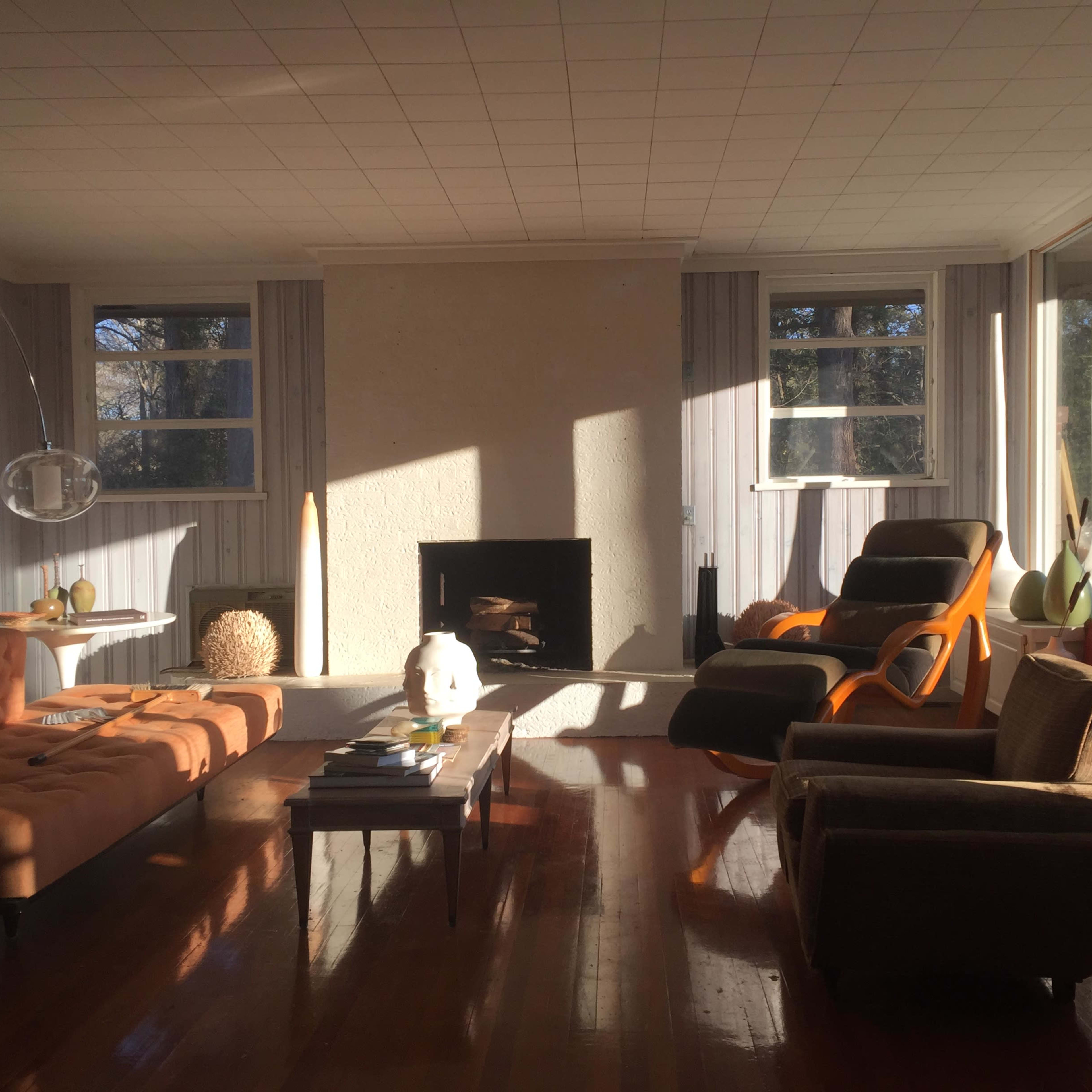 A spacious living room features a fireplace, large windows, and a mix of modern furniture arranged around a coffee table.