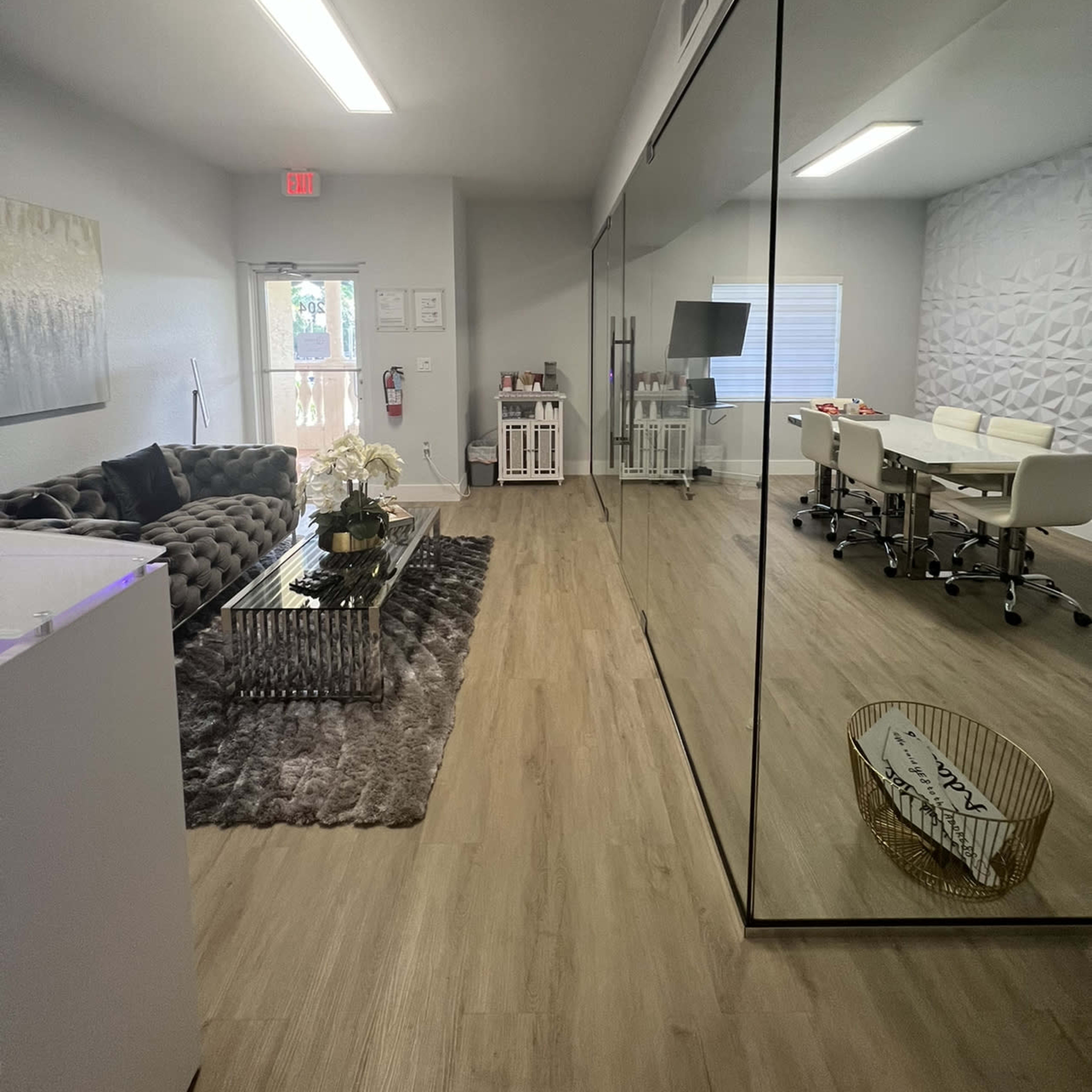 A modern office space featuring a lounge area with a sofa, a glass-walled meeting room, and light-colored walls with wooden flooring.