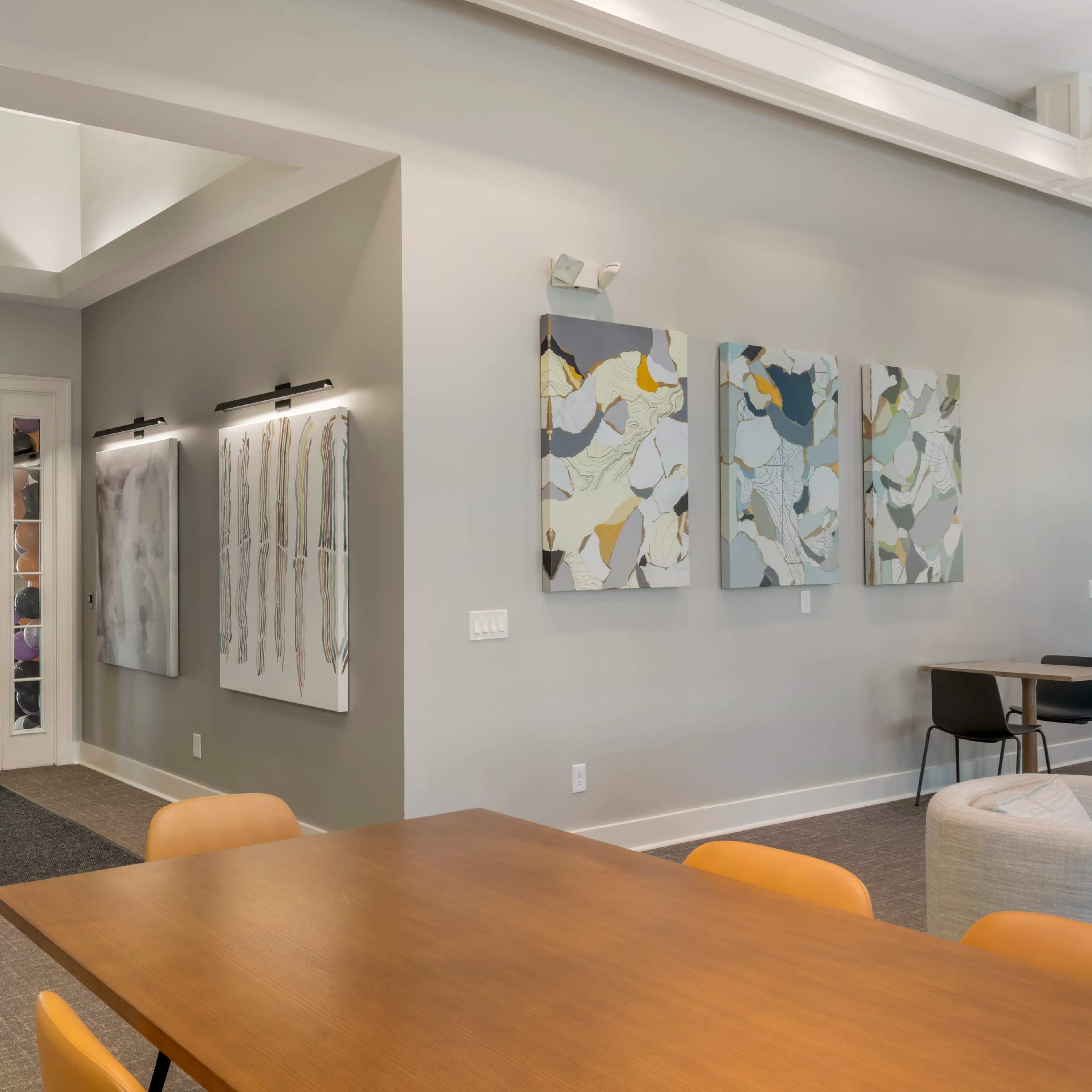 A spacious indoor area featuring two sets of glass doors, abstract artwork on the walls, and a wooden table with orange chairs.
