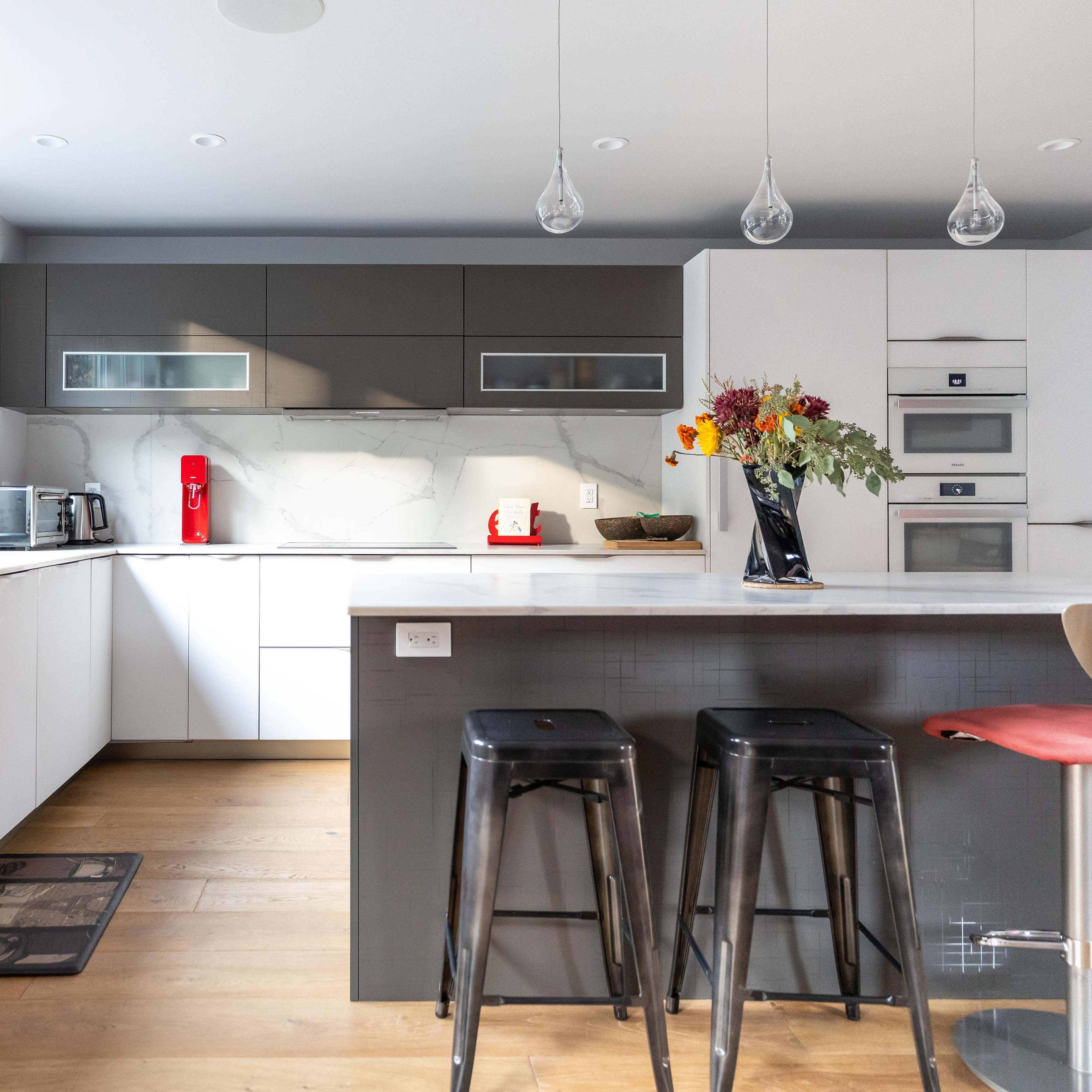 A modern kitchen with white and gray cabinetry, stainless steel appliances, and a central island with bar stools.