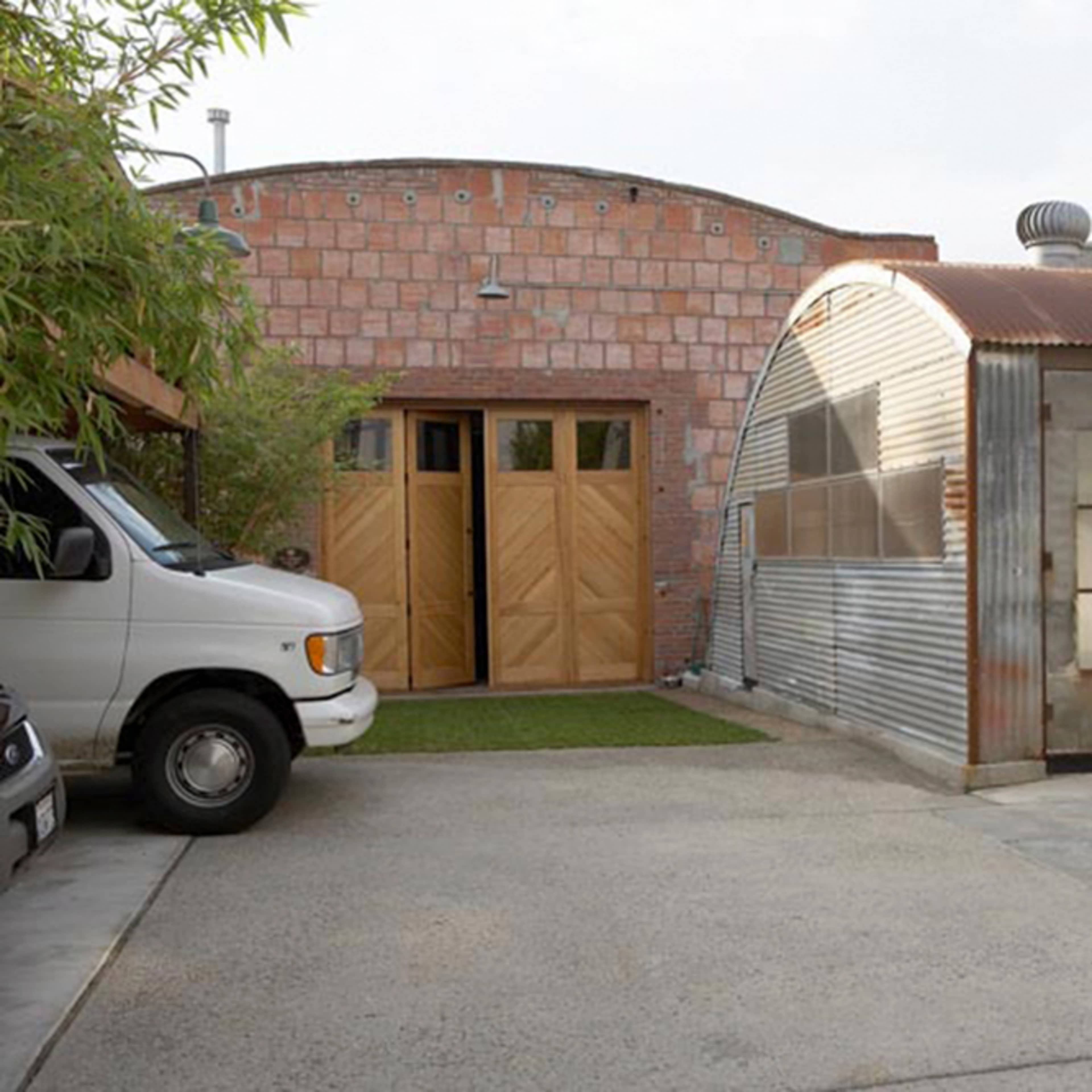 A small, corrugated metal building next to a wooden structure in an outdoor space with concrete and grass.