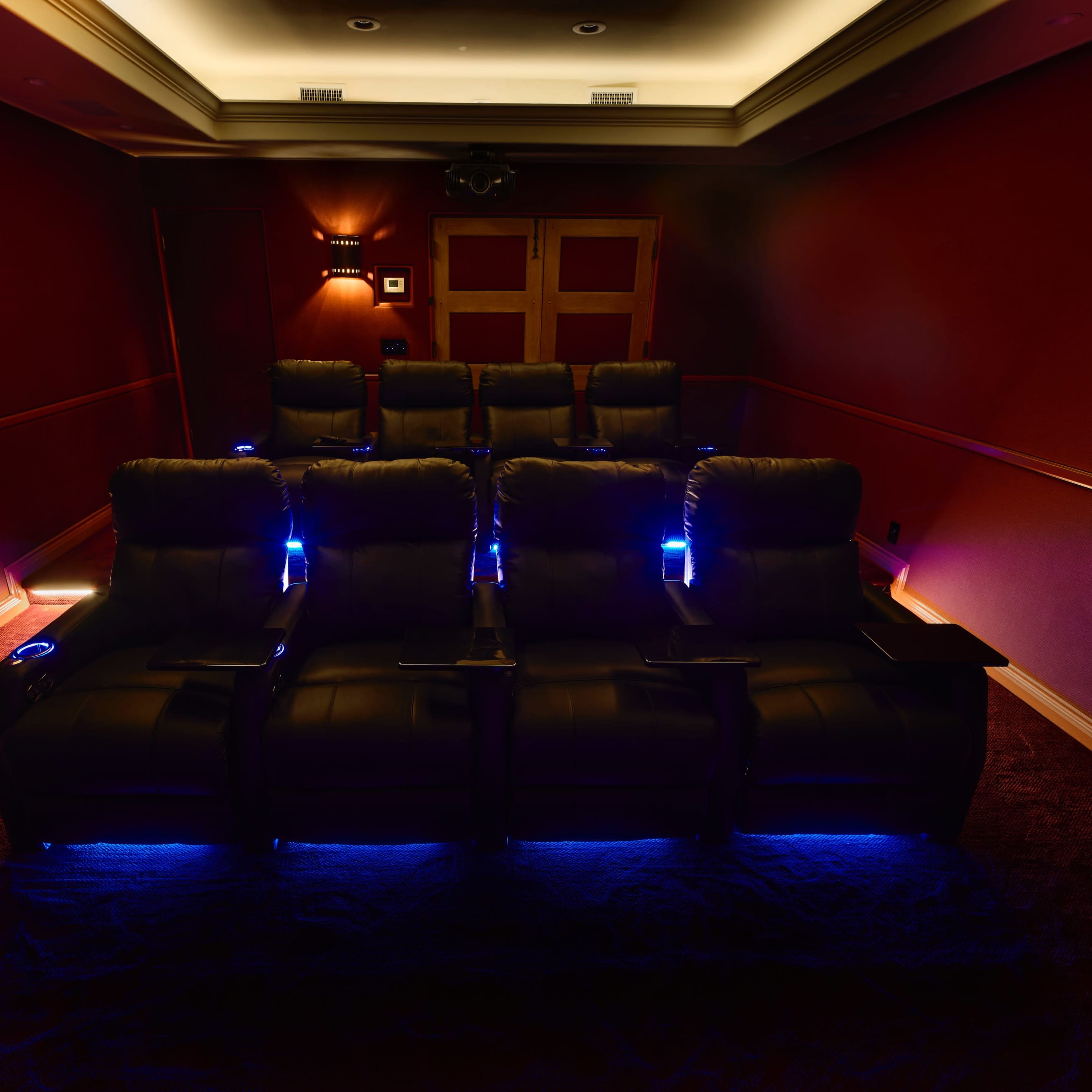 A dark, private home theater with six black reclining seats illuminated by soft blue lights.