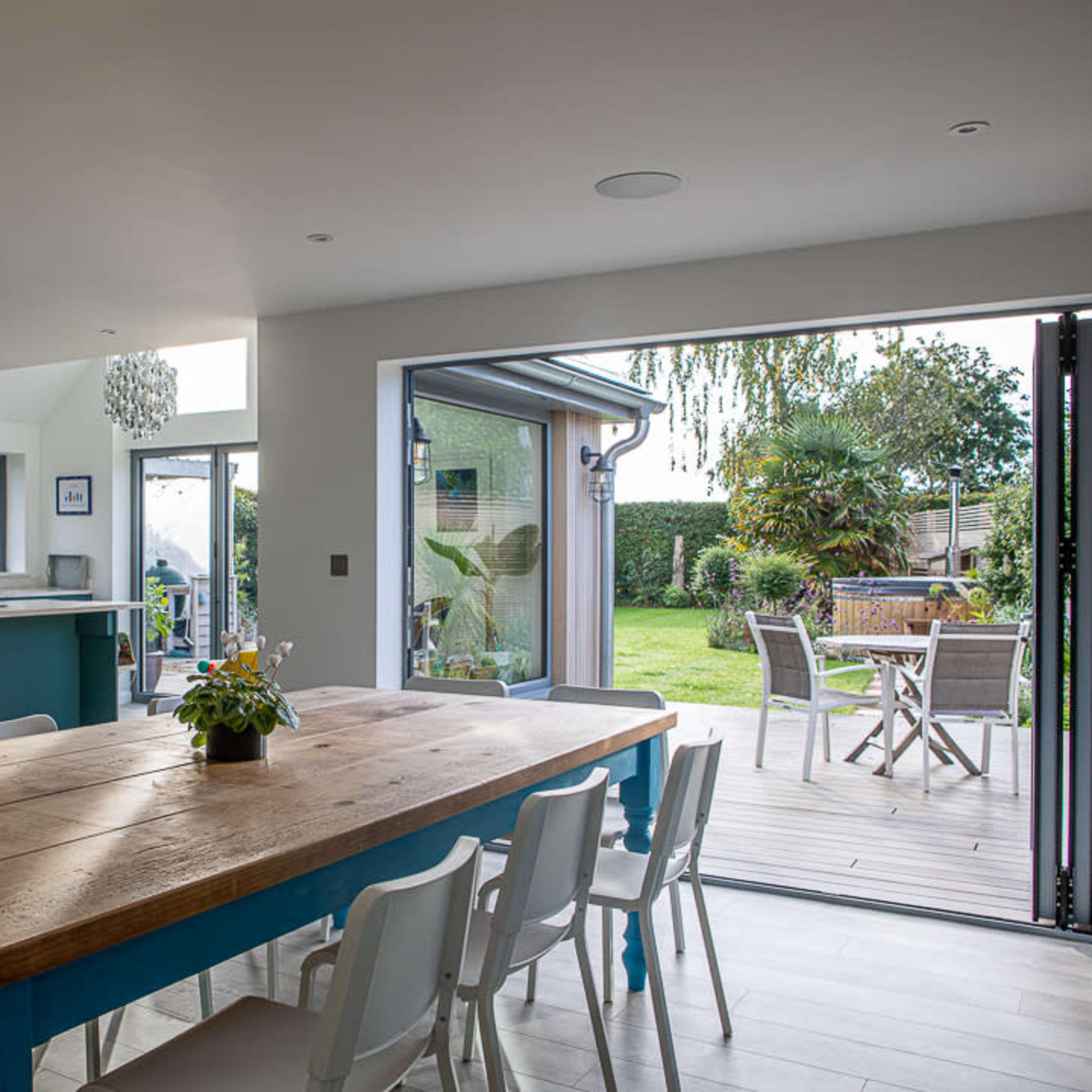 A spacious dining area features a large wooden table surrounded by white chairs, with a view of a backyard through glass doors.