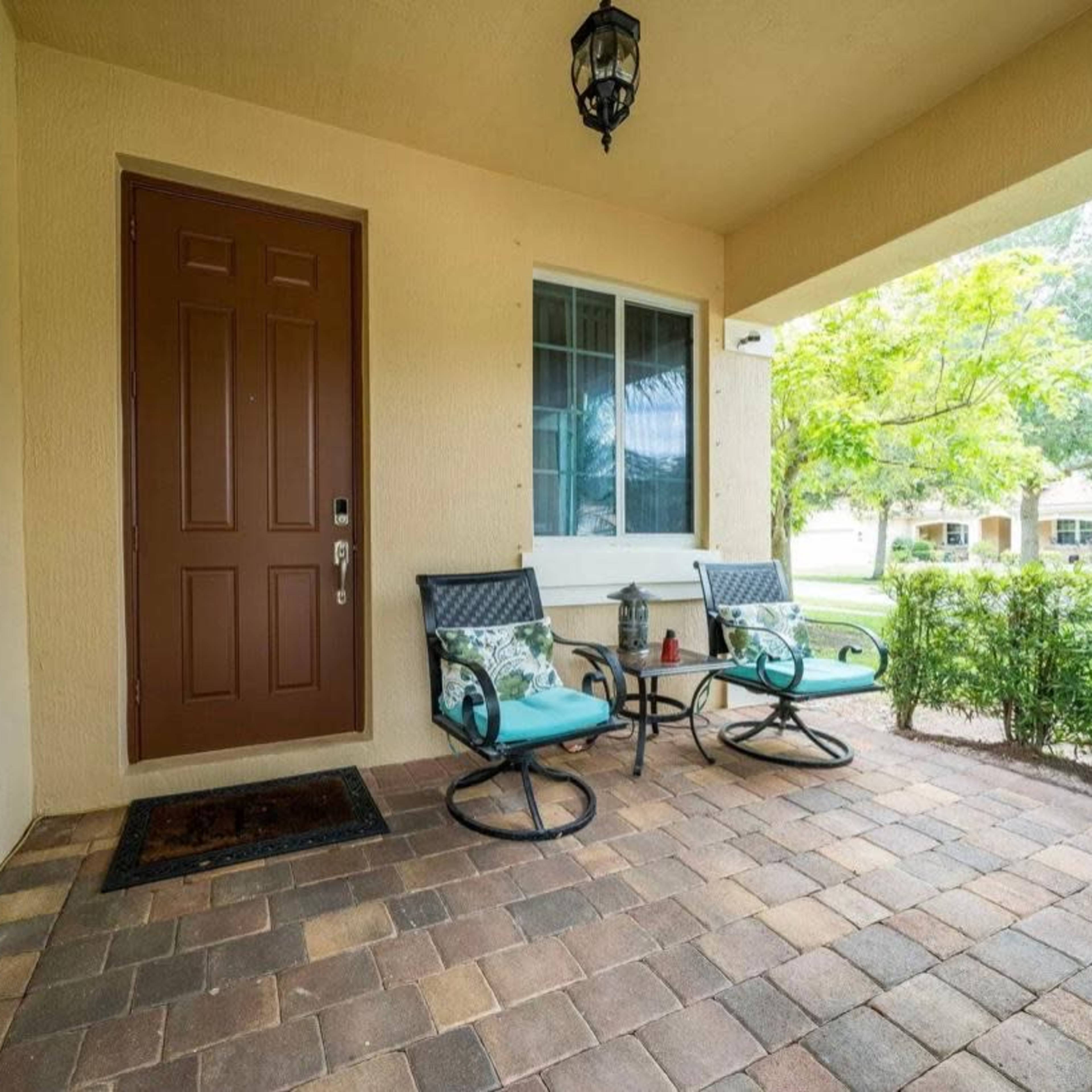A small porch with two chairs and a door, surrounded by greenery.