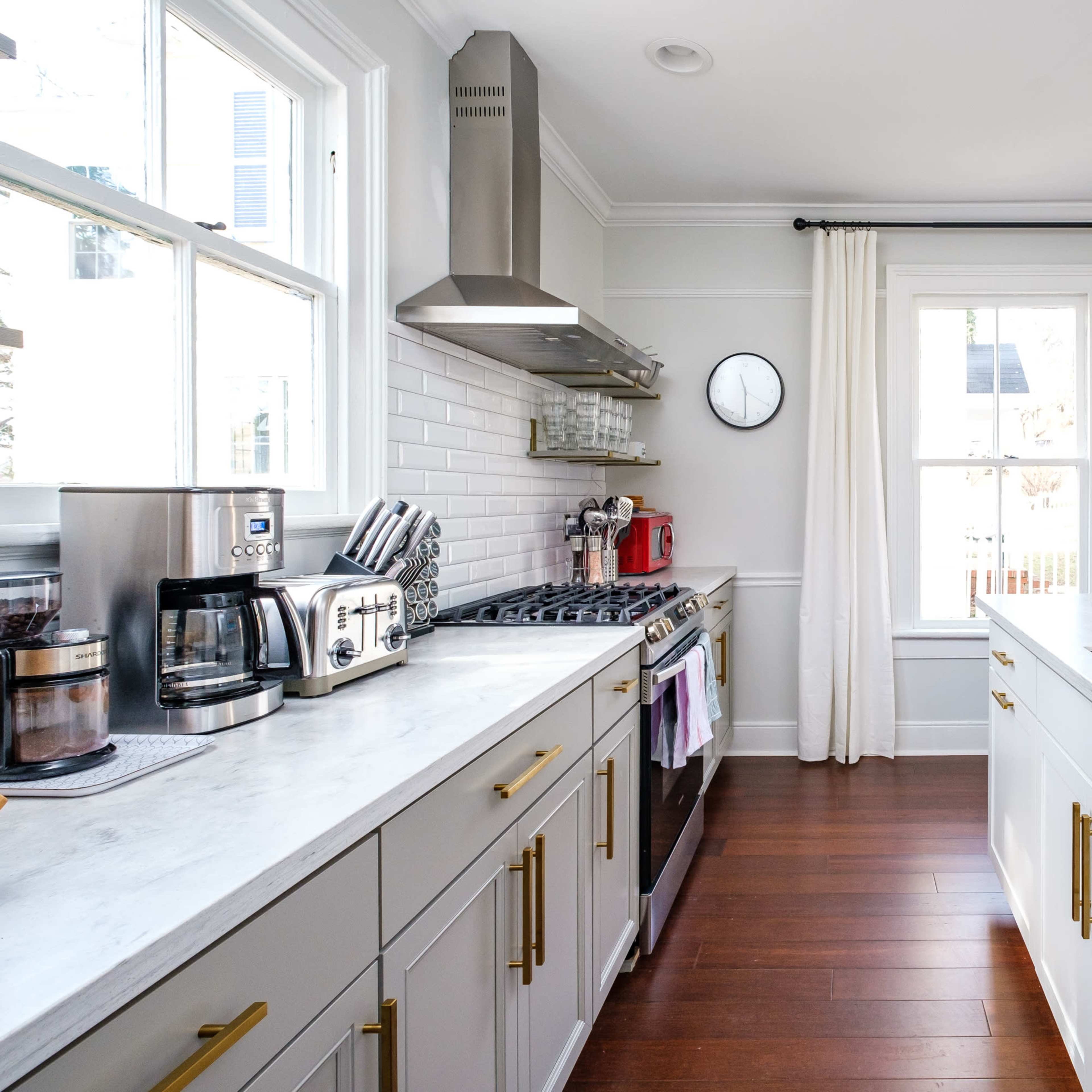 A modern kitchen featuring stainless steel appliances, a marble countertop, and wooden flooring, with large windows allowing natural light.