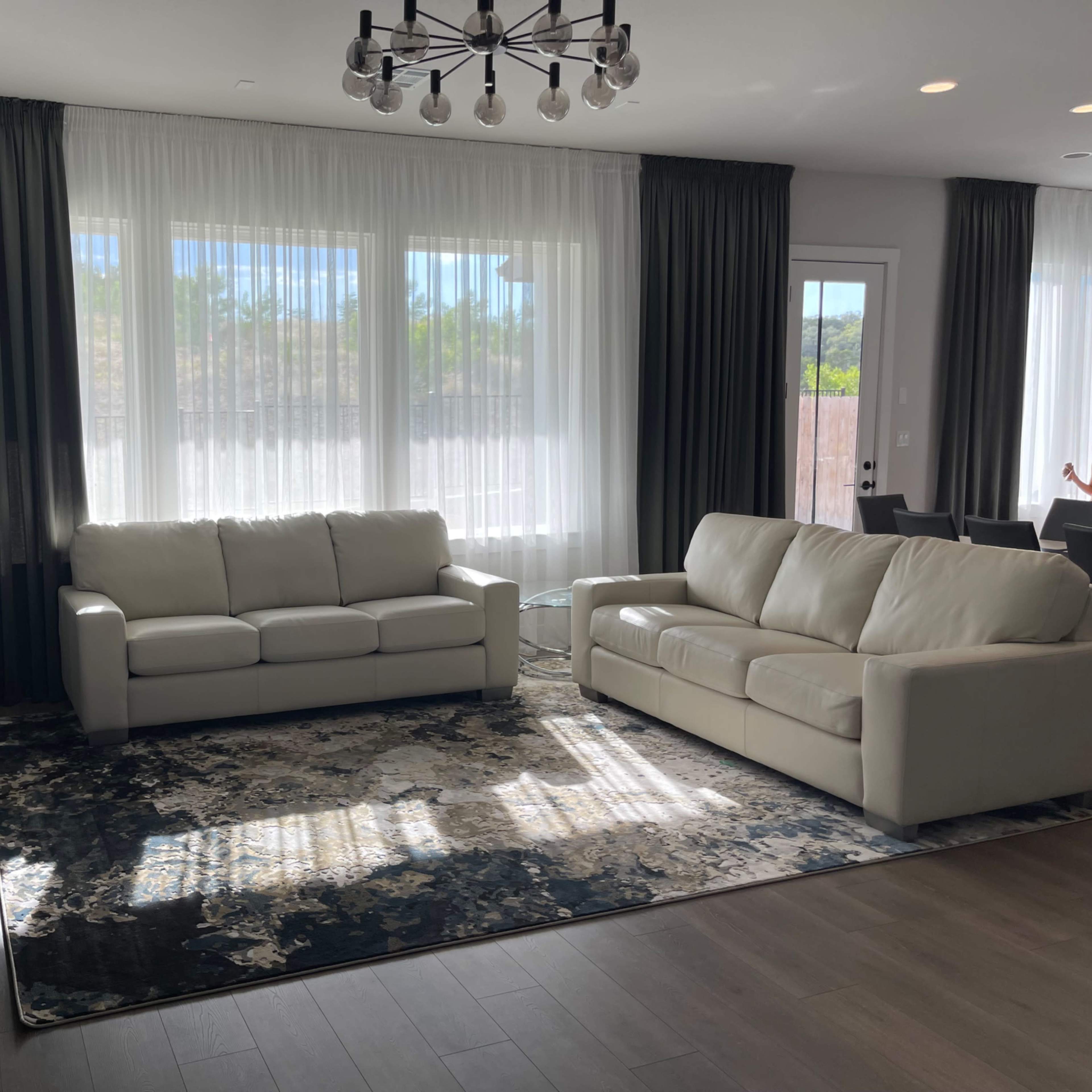 The living room features two white sofas, a dark area rug, a television on a black cabinet, and large windows with sheer curtains.