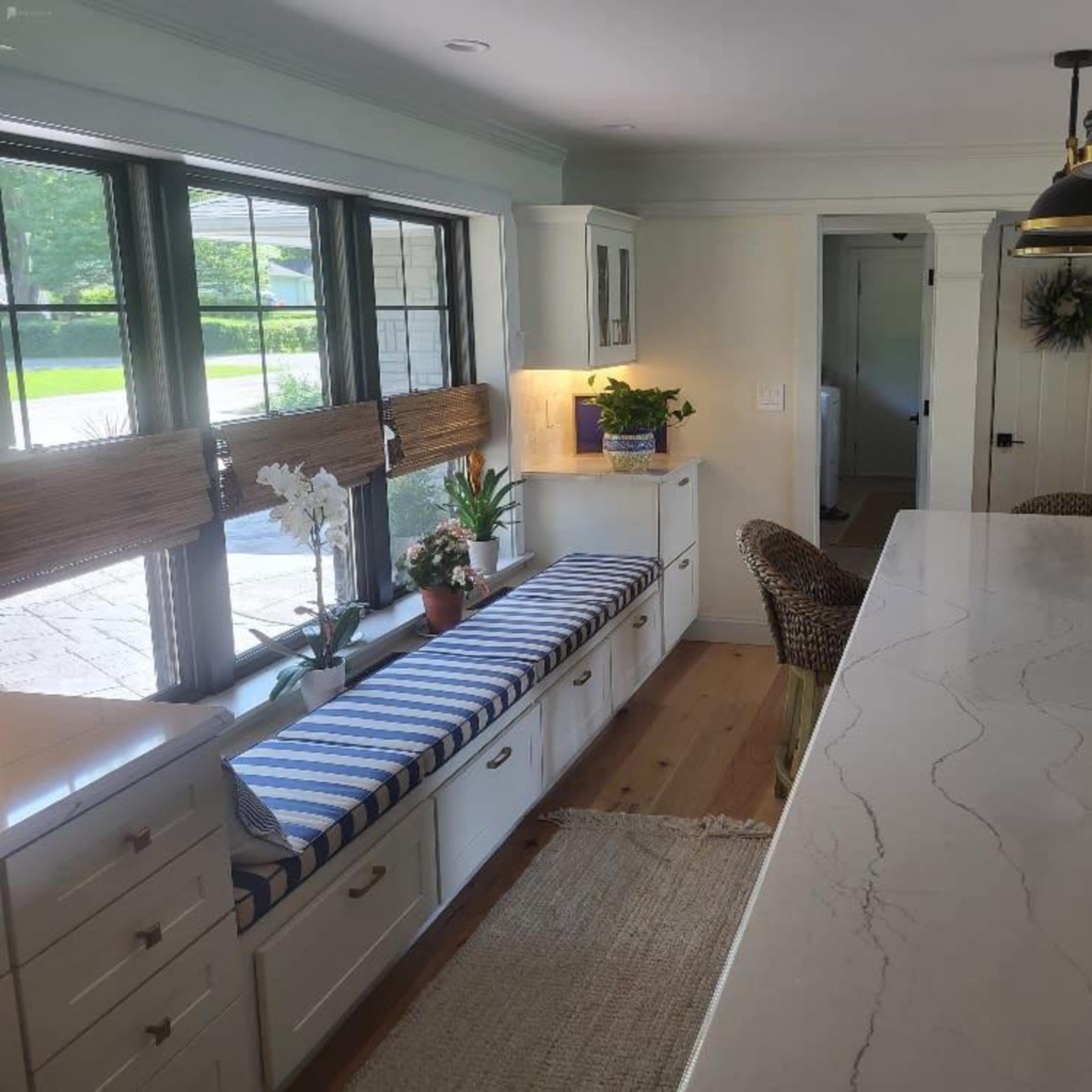 A kitchen interior featuring a marble countertop, a window bench with blue and white striped cushions, and a view of greenery outside.
