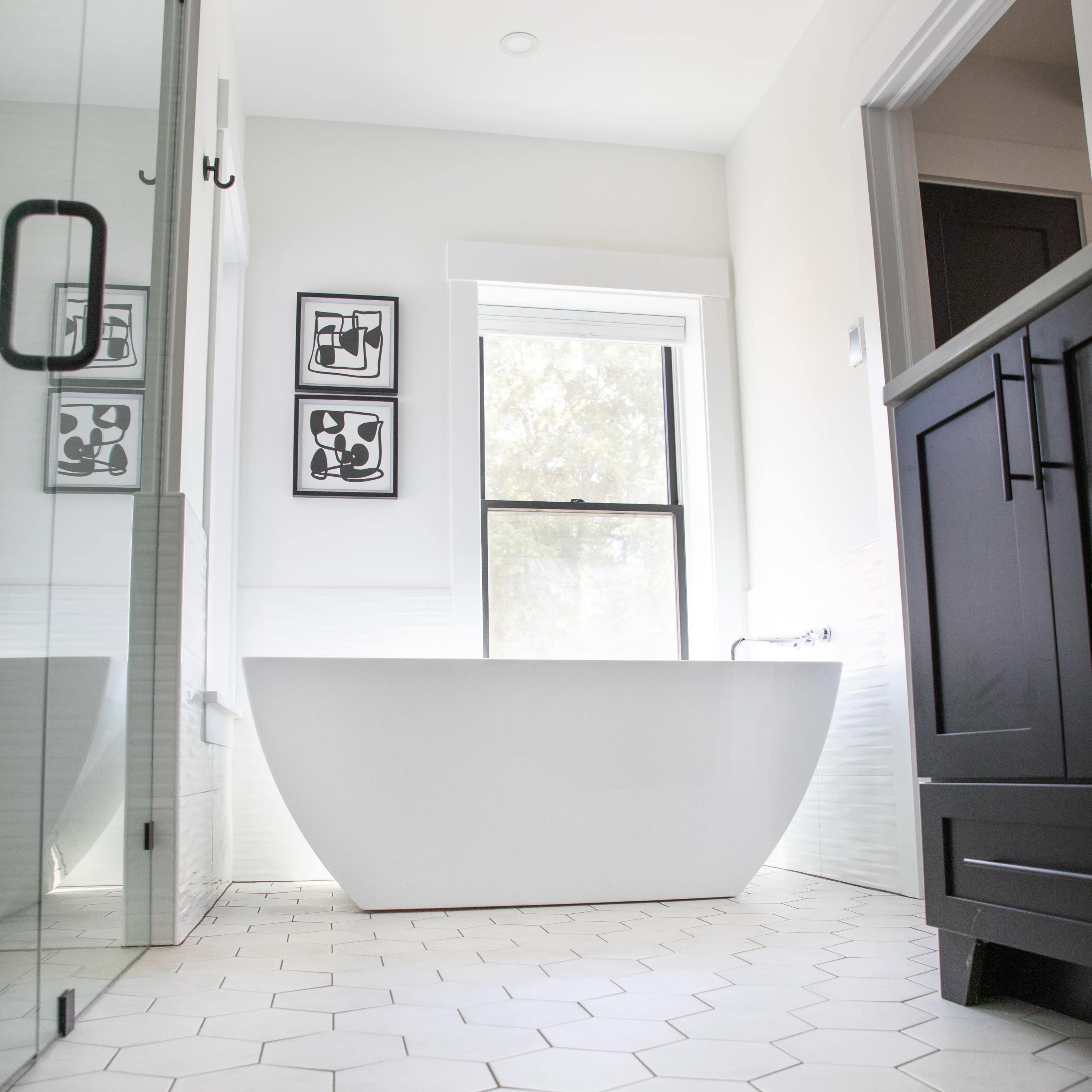 A modern bathroom featuring a freestanding white bathtub, hexagonal floor tiles, and framed artwork on the walls.