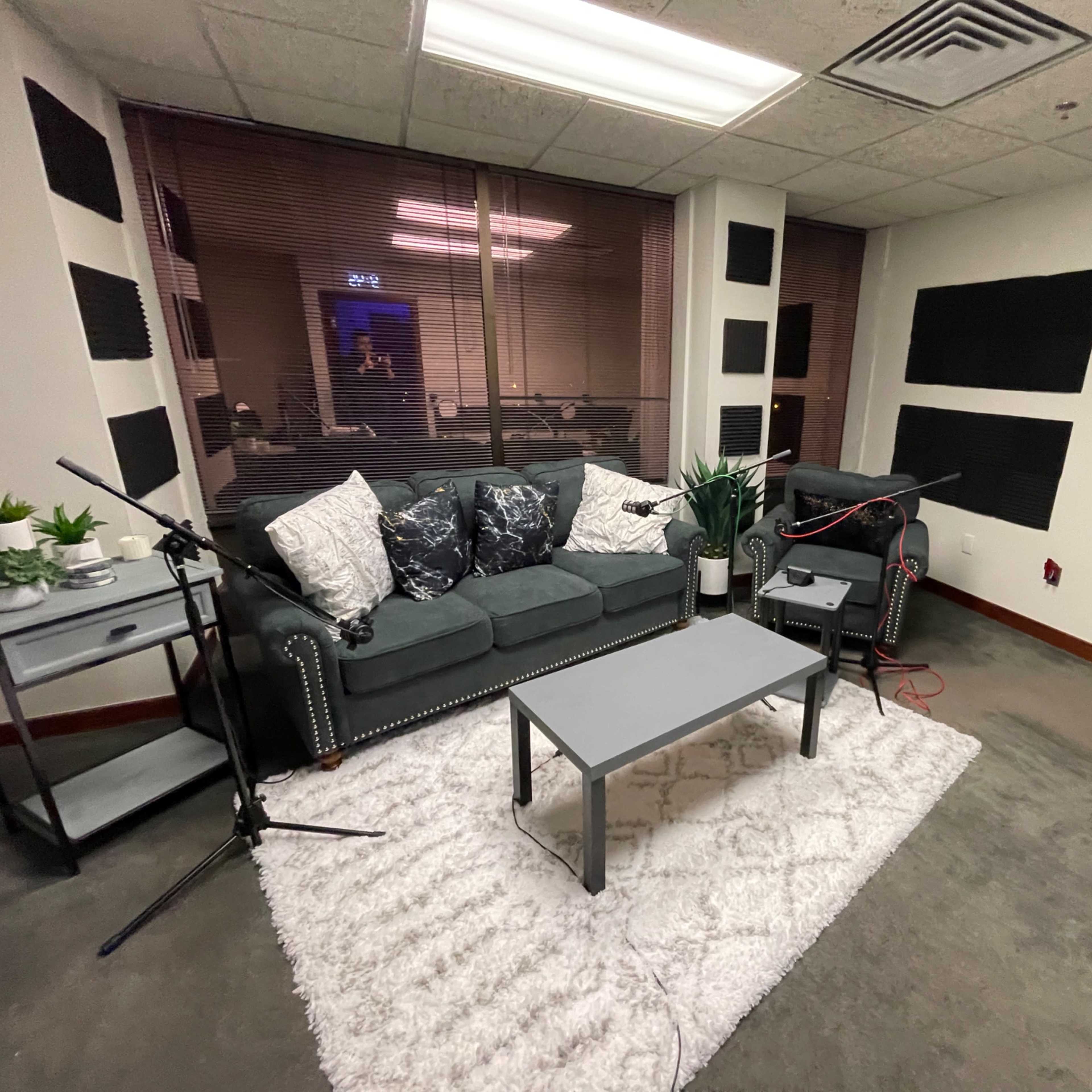 A small recording studio featuring a green couch, a coffee table, and acoustic panels on the walls.