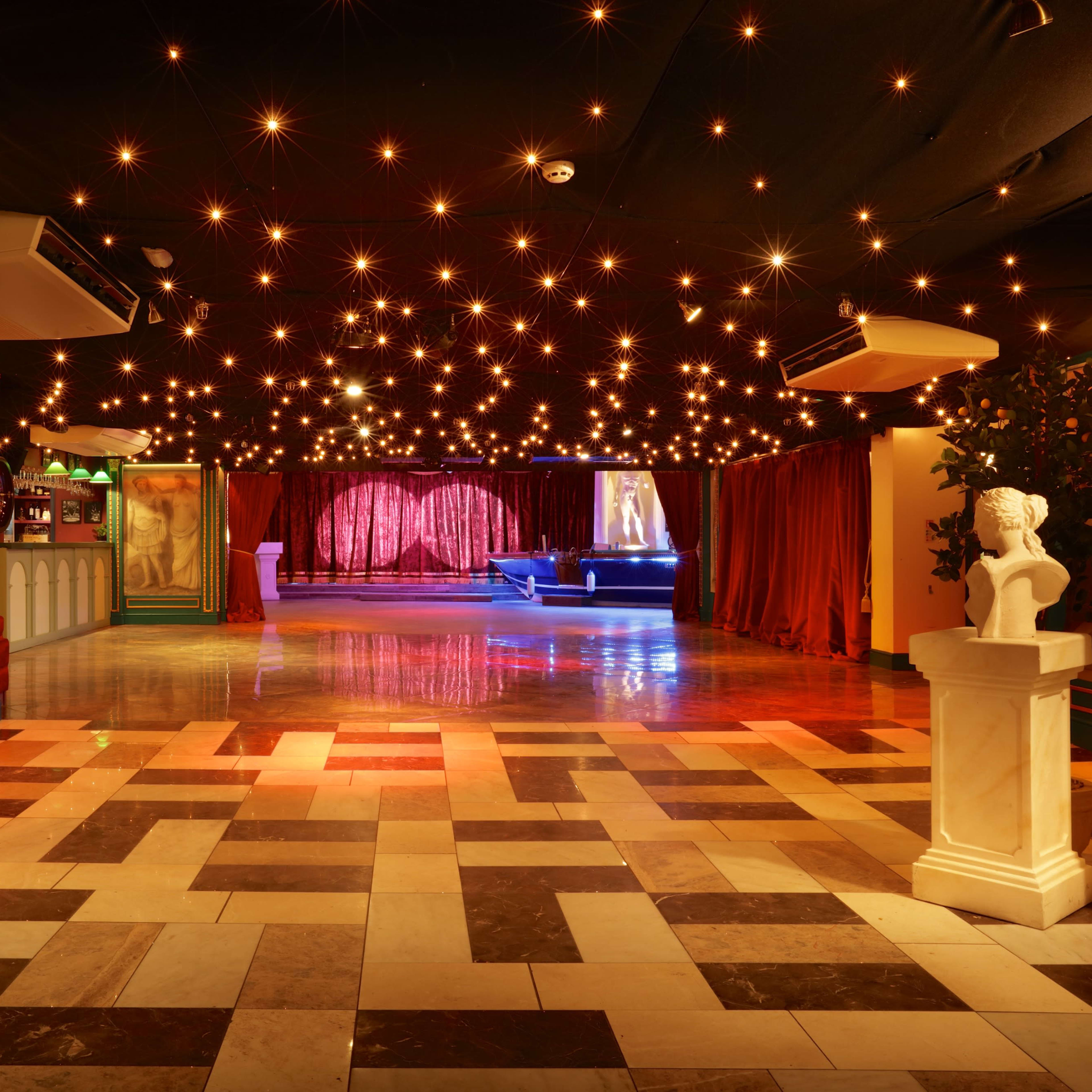 An elegantly designed venue with a checkered floor, decorative walls, and dim lighting featuring a starry ceiling and a stage with red curtains.