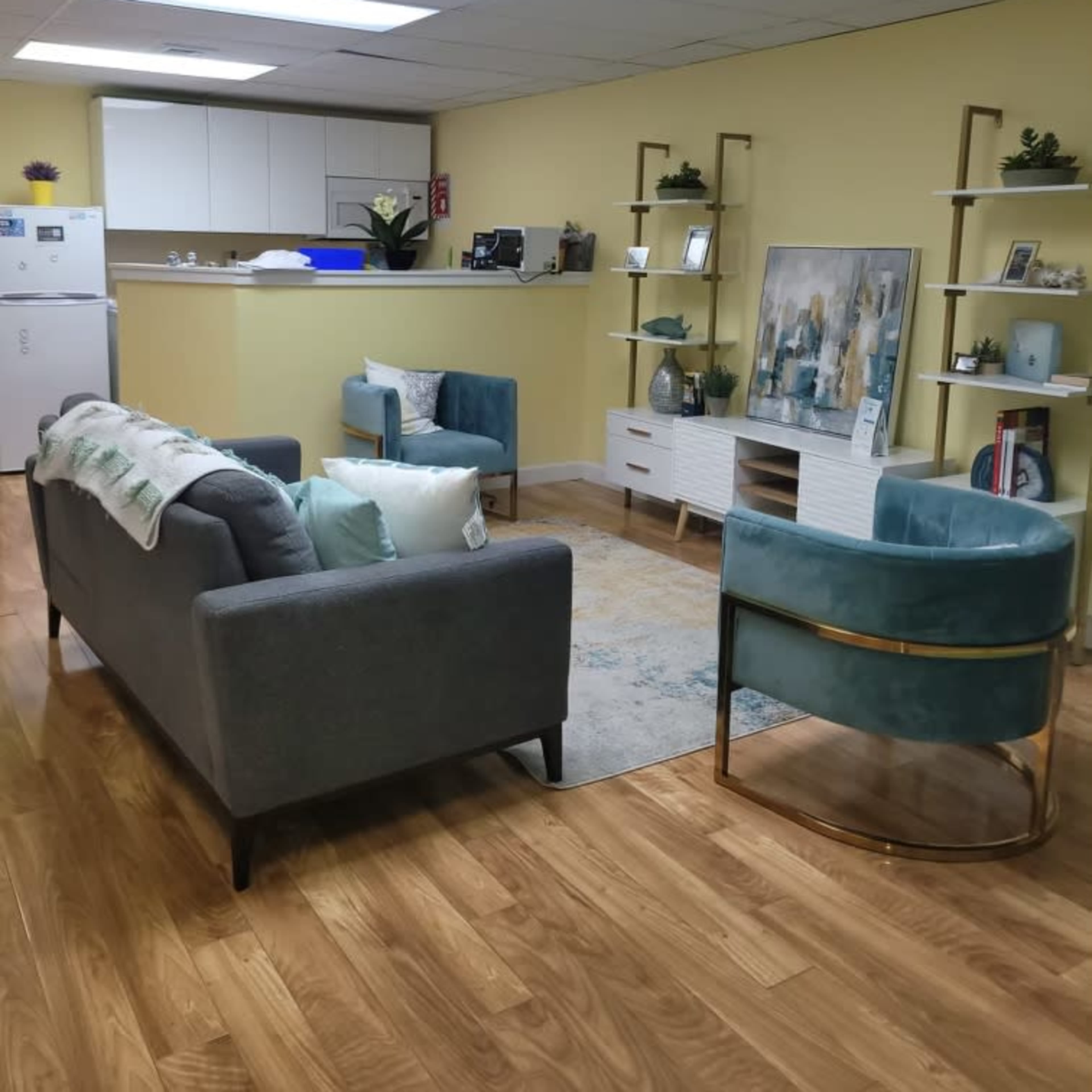 A modern office space with a seating area featuring two armchairs and a sofa, a coffee table, and a kitchenette in the background.