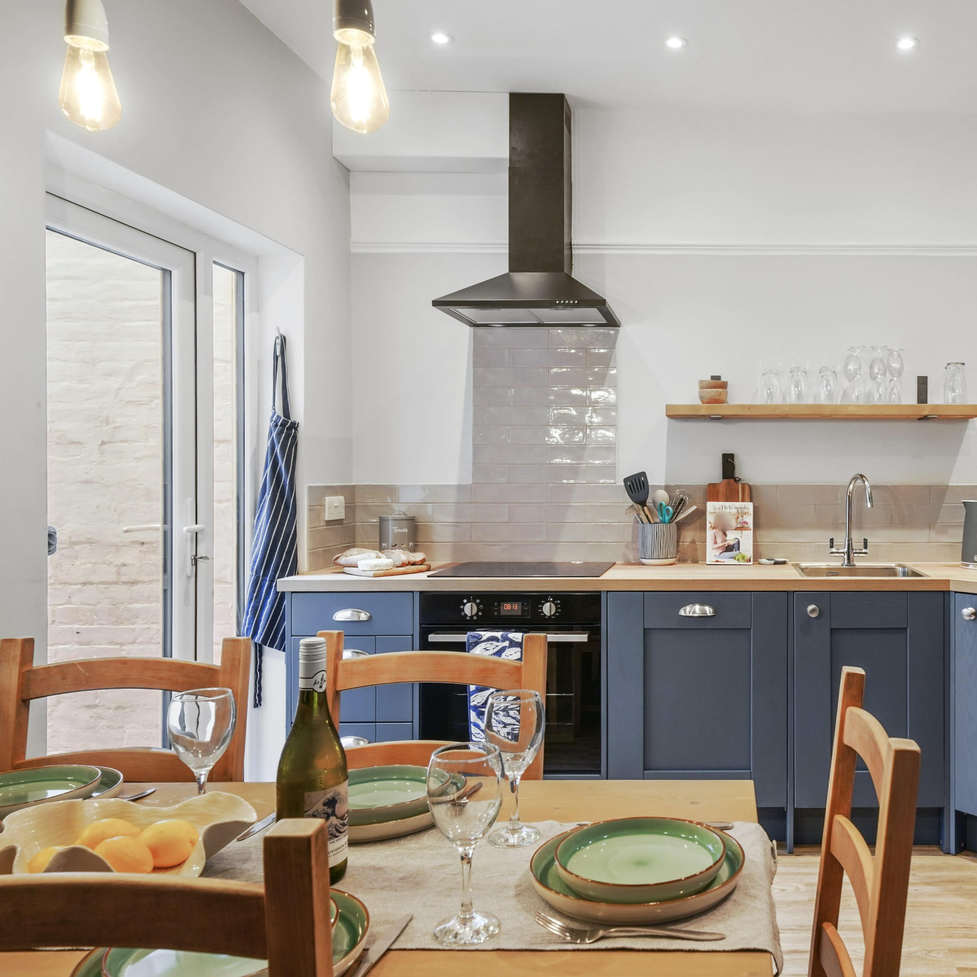 A modern kitchen features blue cabinetry, wooden countertops, and an island, with a dining table set for a meal.