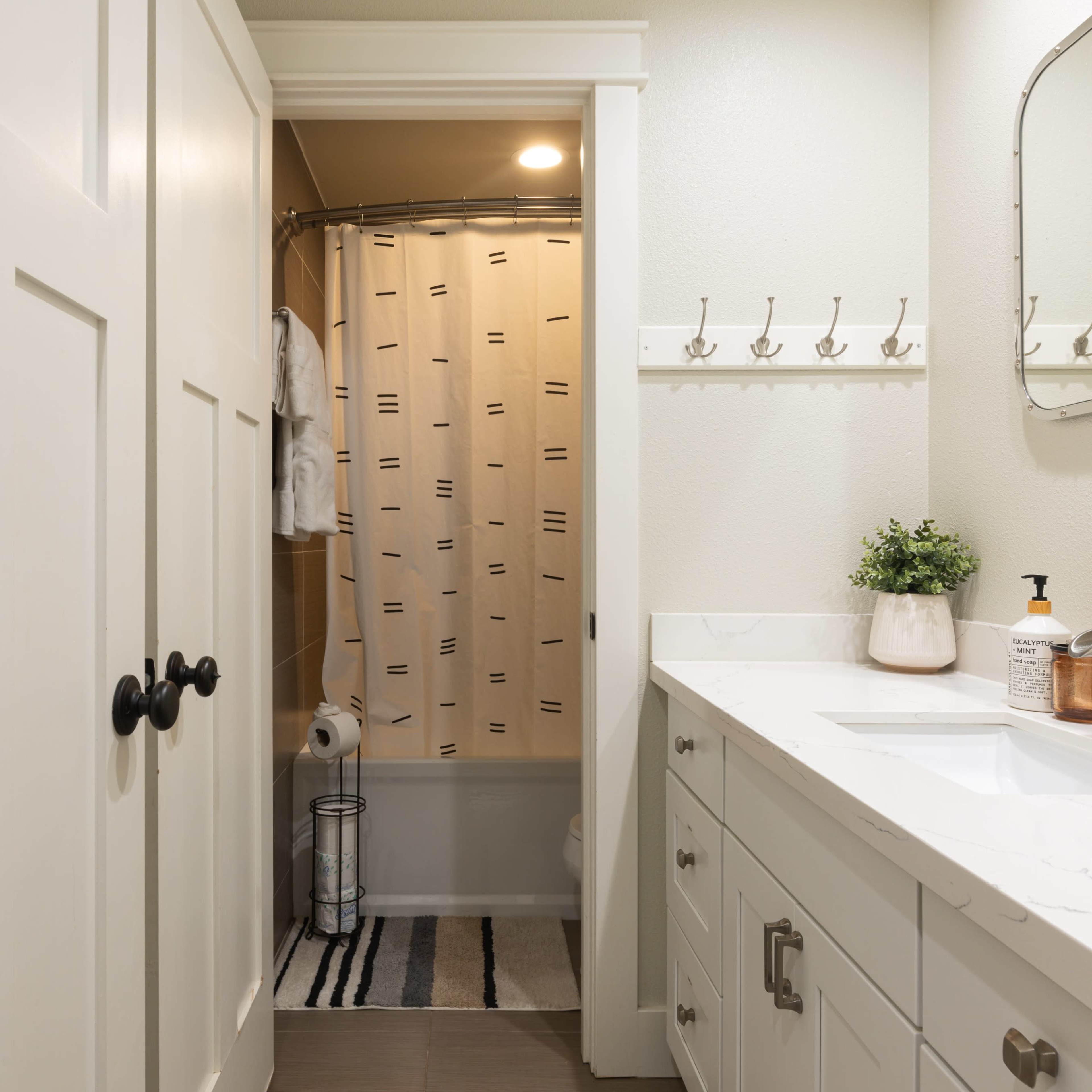 A well-lit bathroom features a shower area with a curtain, a vanity with a sink, and a door leading to an adjacent space.