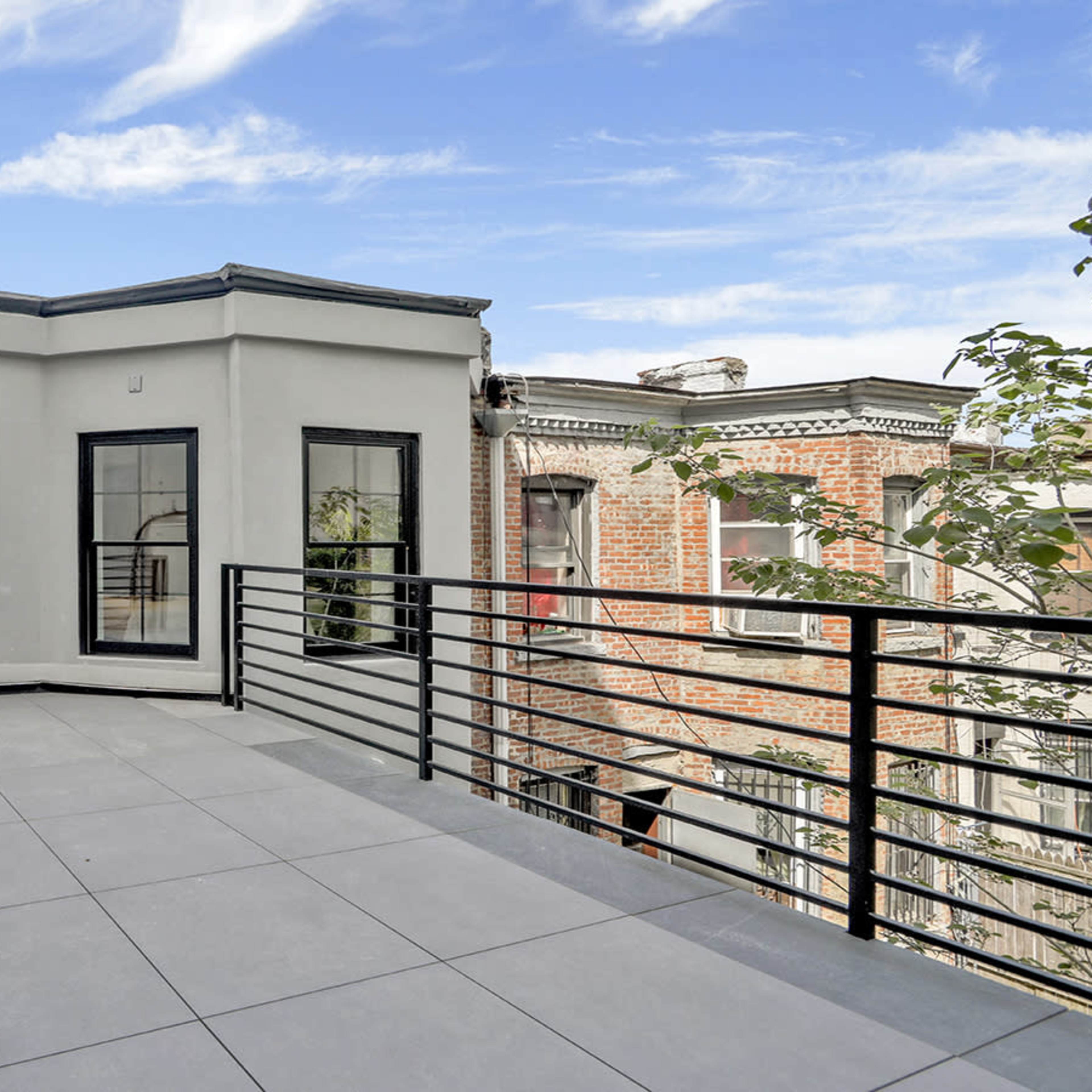 A flat rooftop terrace features modern railing and large windows overlooking adjacent buildings.