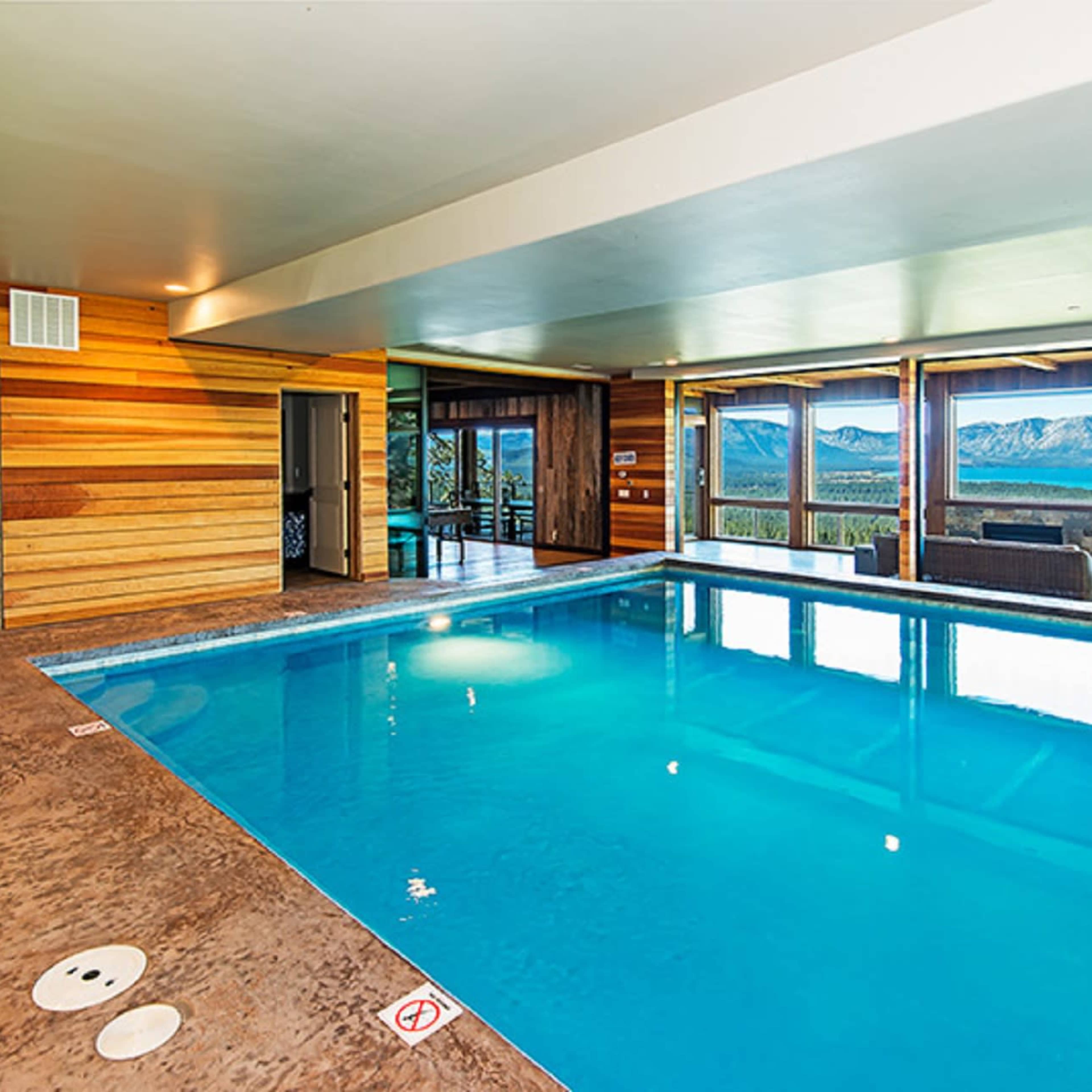 An indoor swimming pool surrounded by large windows offering a view of mountains.