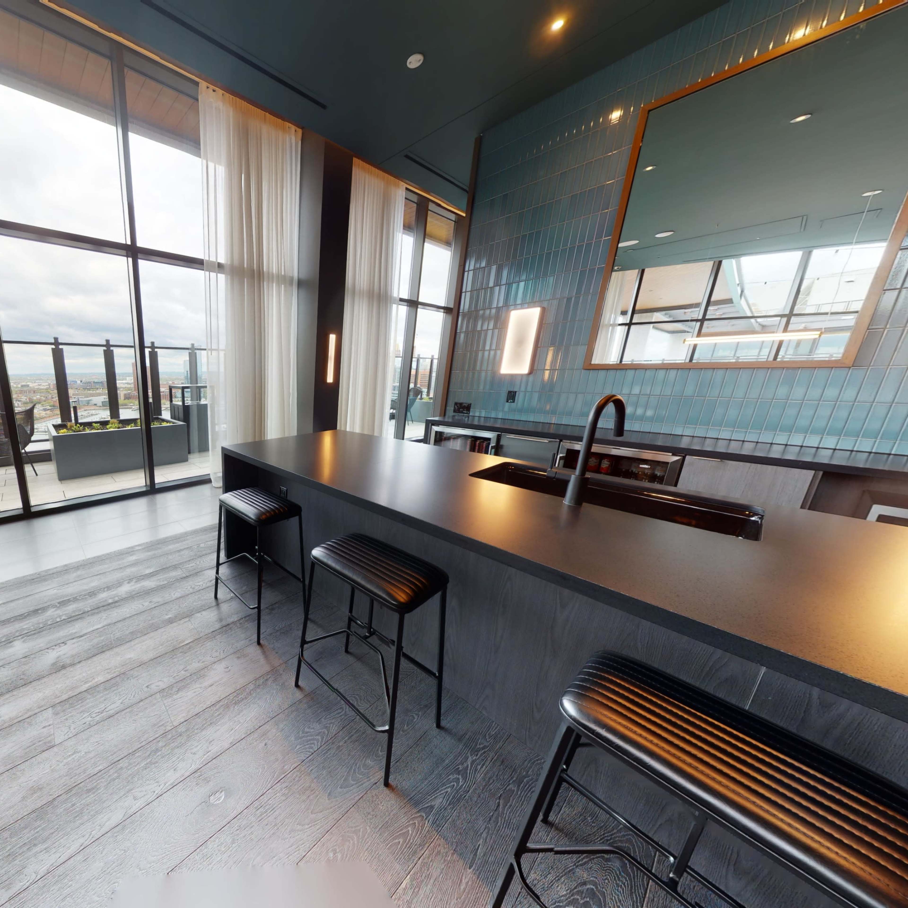 A modern kitchen features a large island with bar stools and floor-to-ceiling windows overlooking a cityscape.