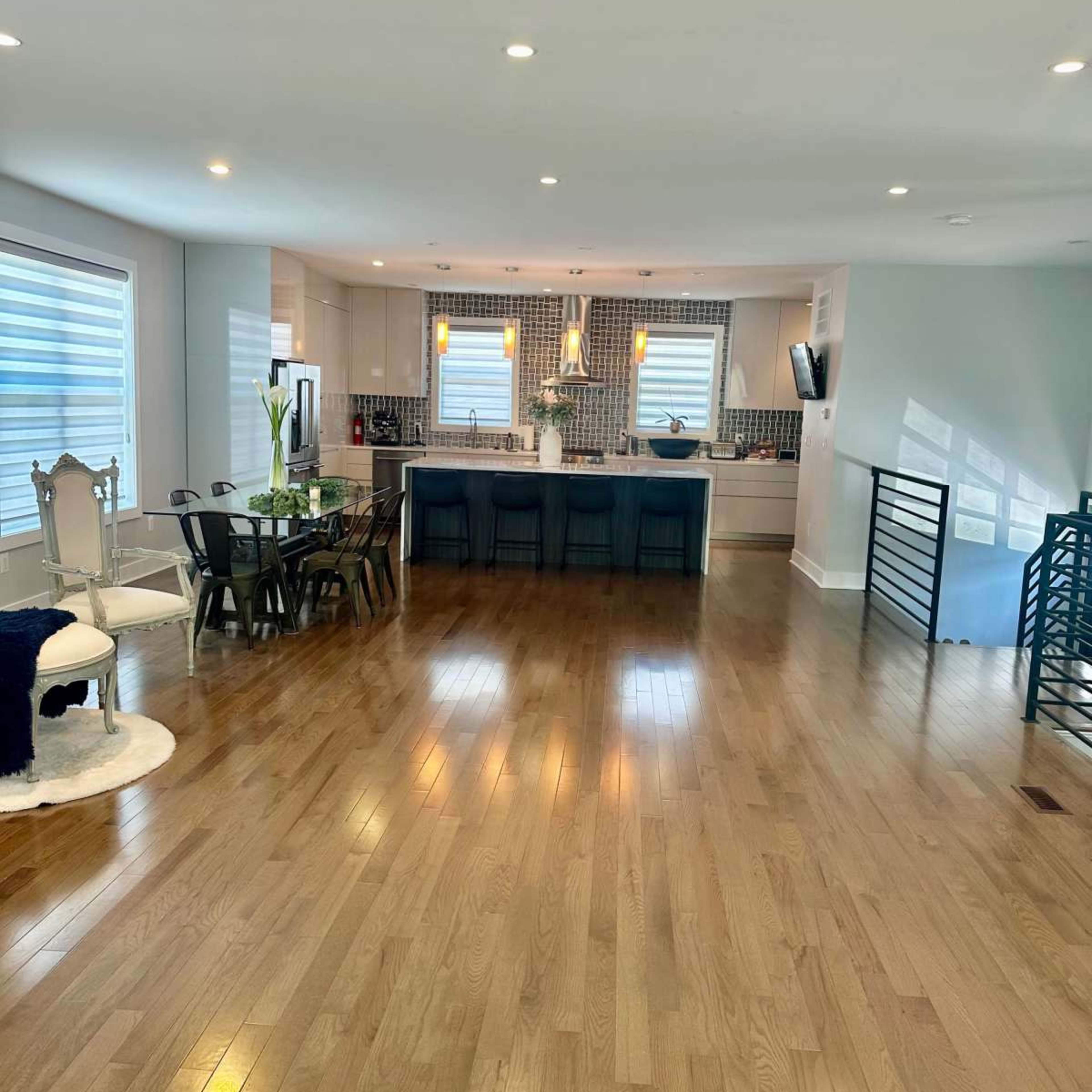 A modern, open-concept living space featuring a kitchen with a central island, a dining area with a table, and hardwood flooring.