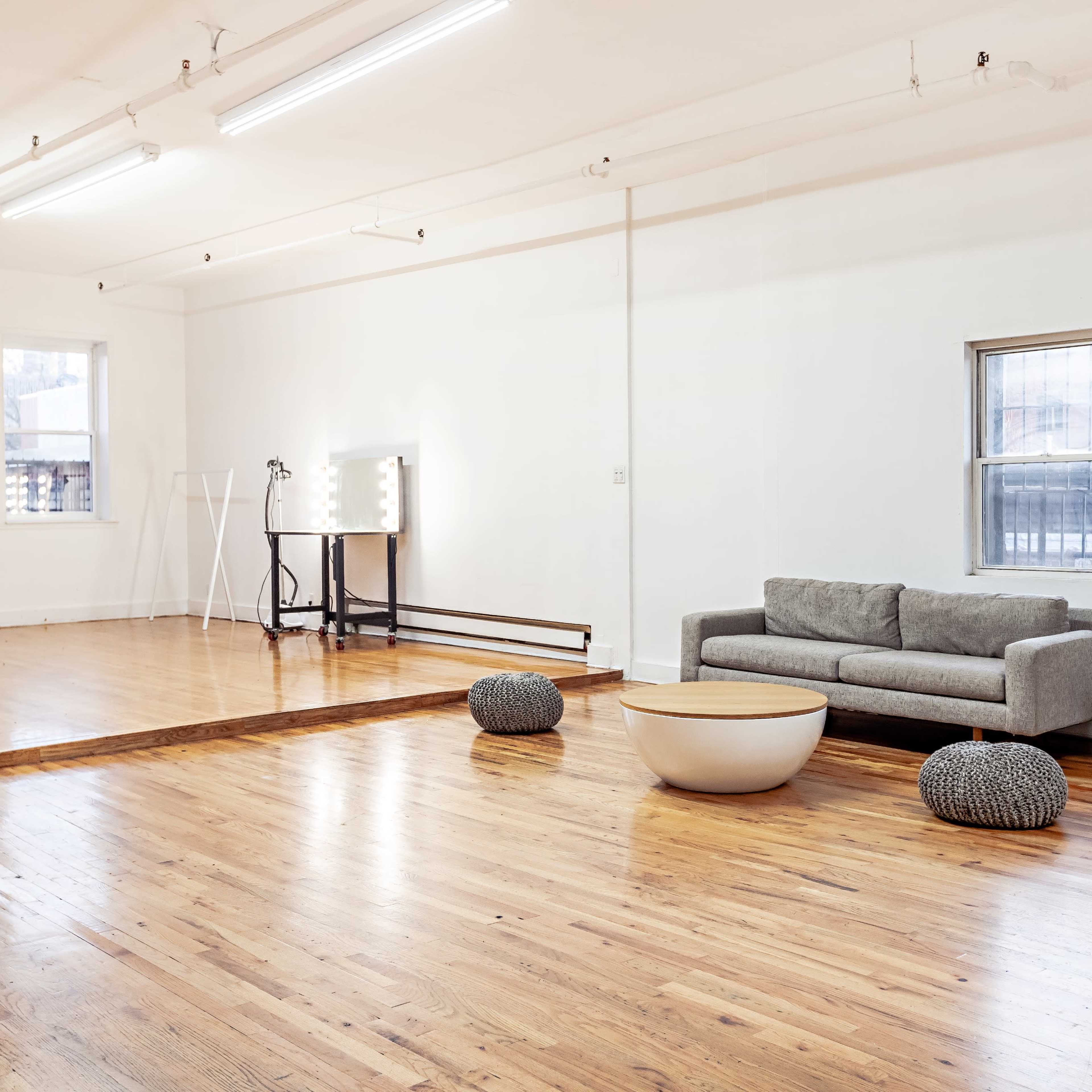 A spacious, minimalist room with hardwood floors, featuring a grey sofa, a round coffee table, and two decorative poufs.