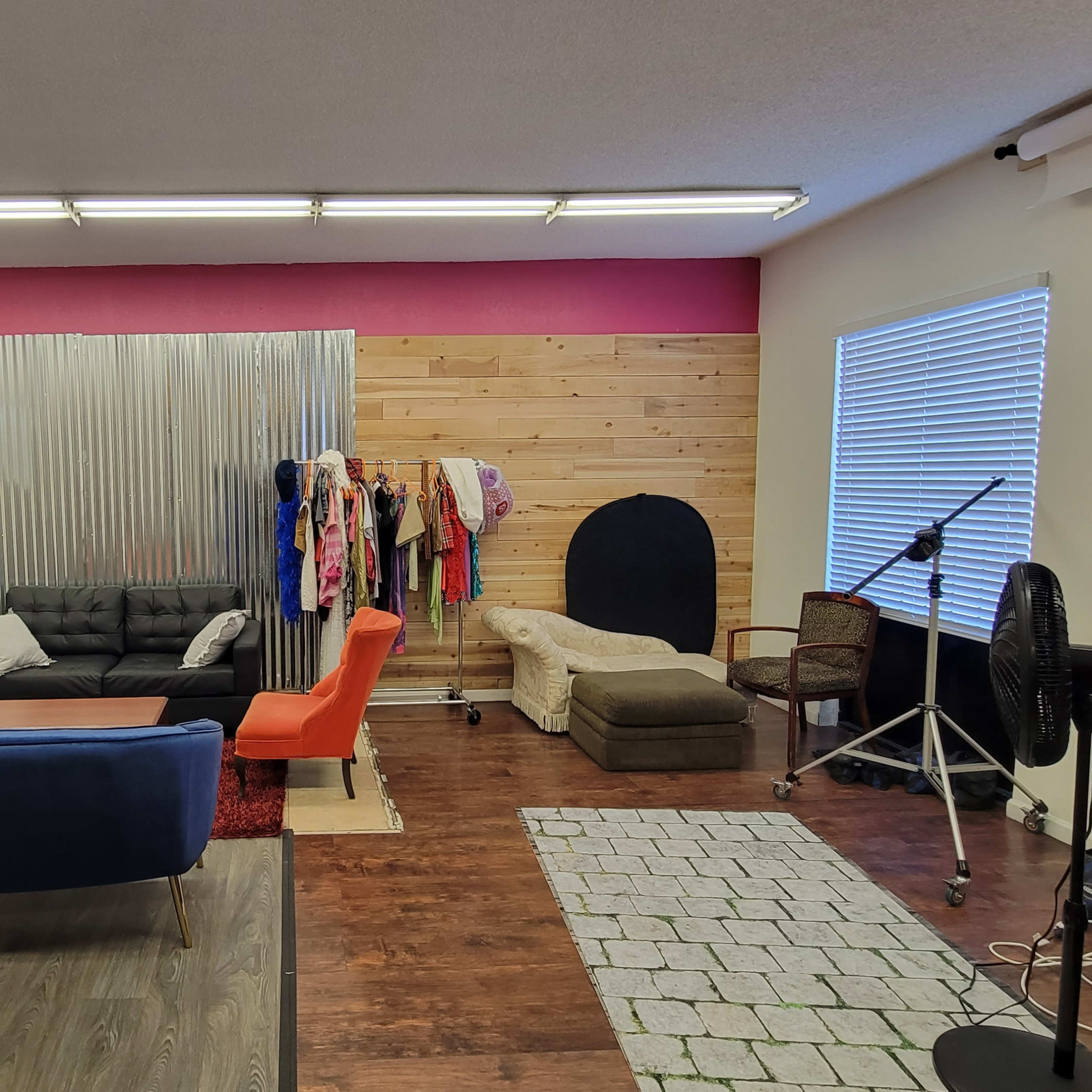 A studio space with several seating areas, a clothing rack, various decorative elements, and a fan in the corner.