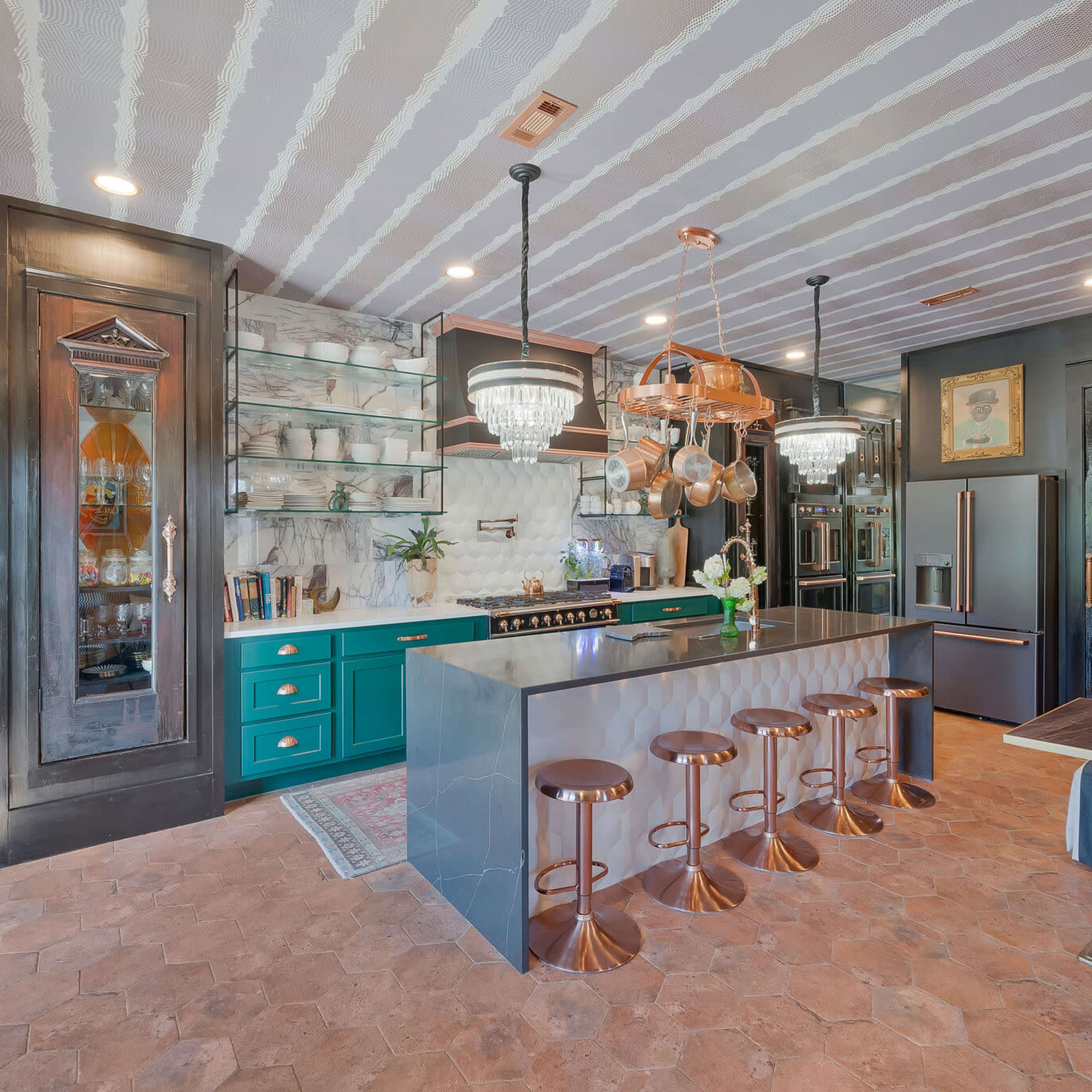A modern kitchen with a dark teal island, pendant lights, and bar stools arranged around a countertop.