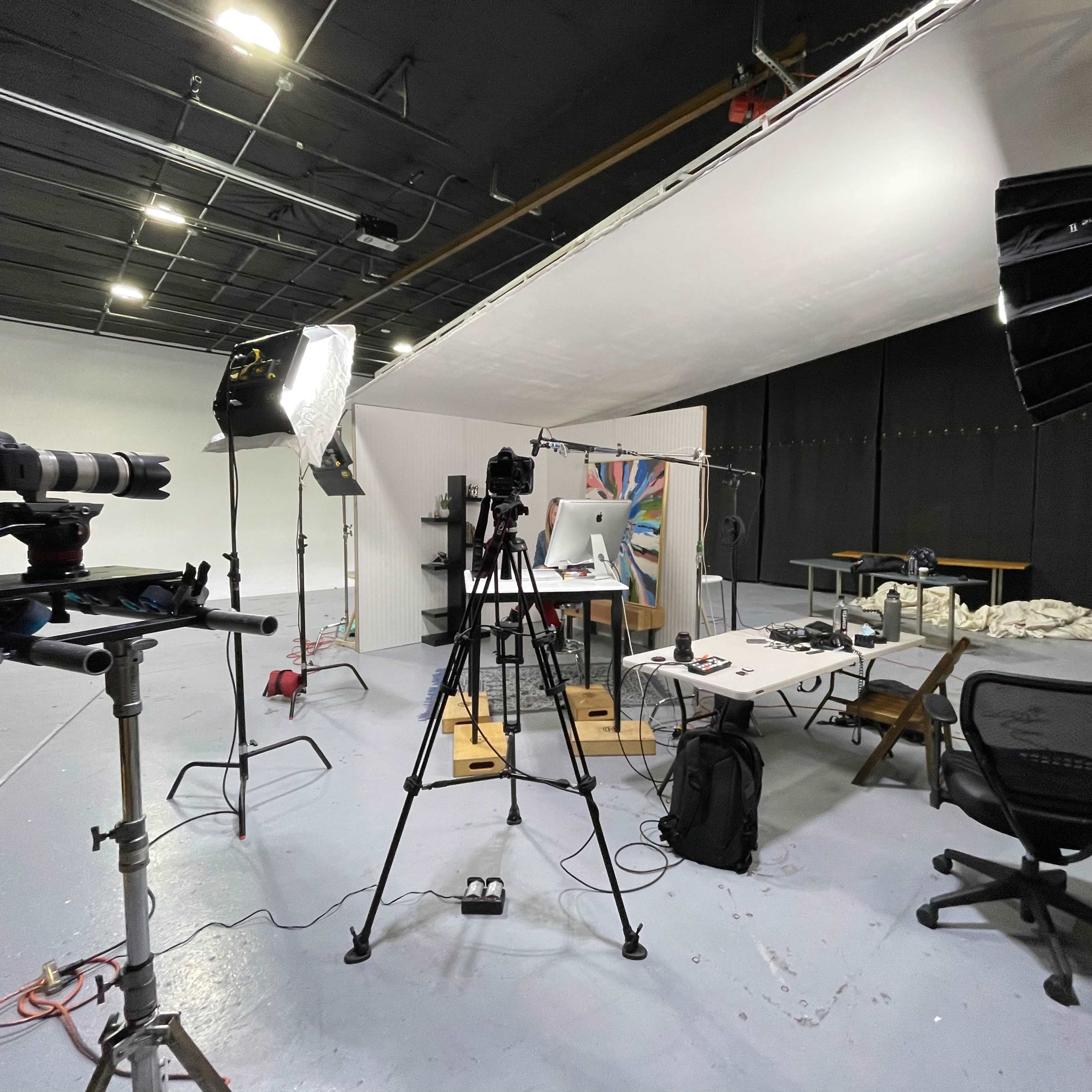 A photography studio with several cameras, lighting equipment, and a work table set up against a plain background.