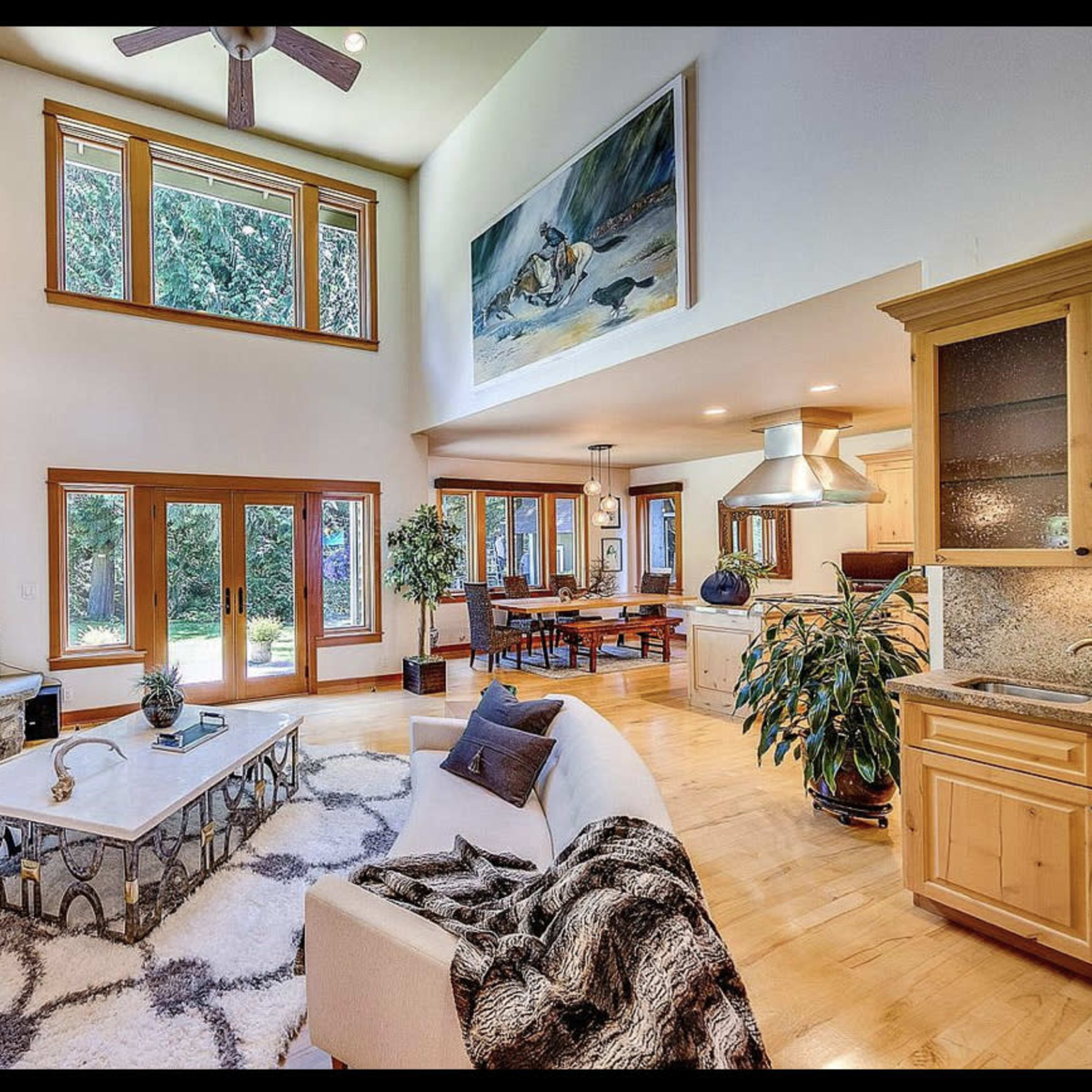 A spacious living room featuring a large stone fireplace, hardwood flooring, a white sofa, and large windows allowing natural light to enter.