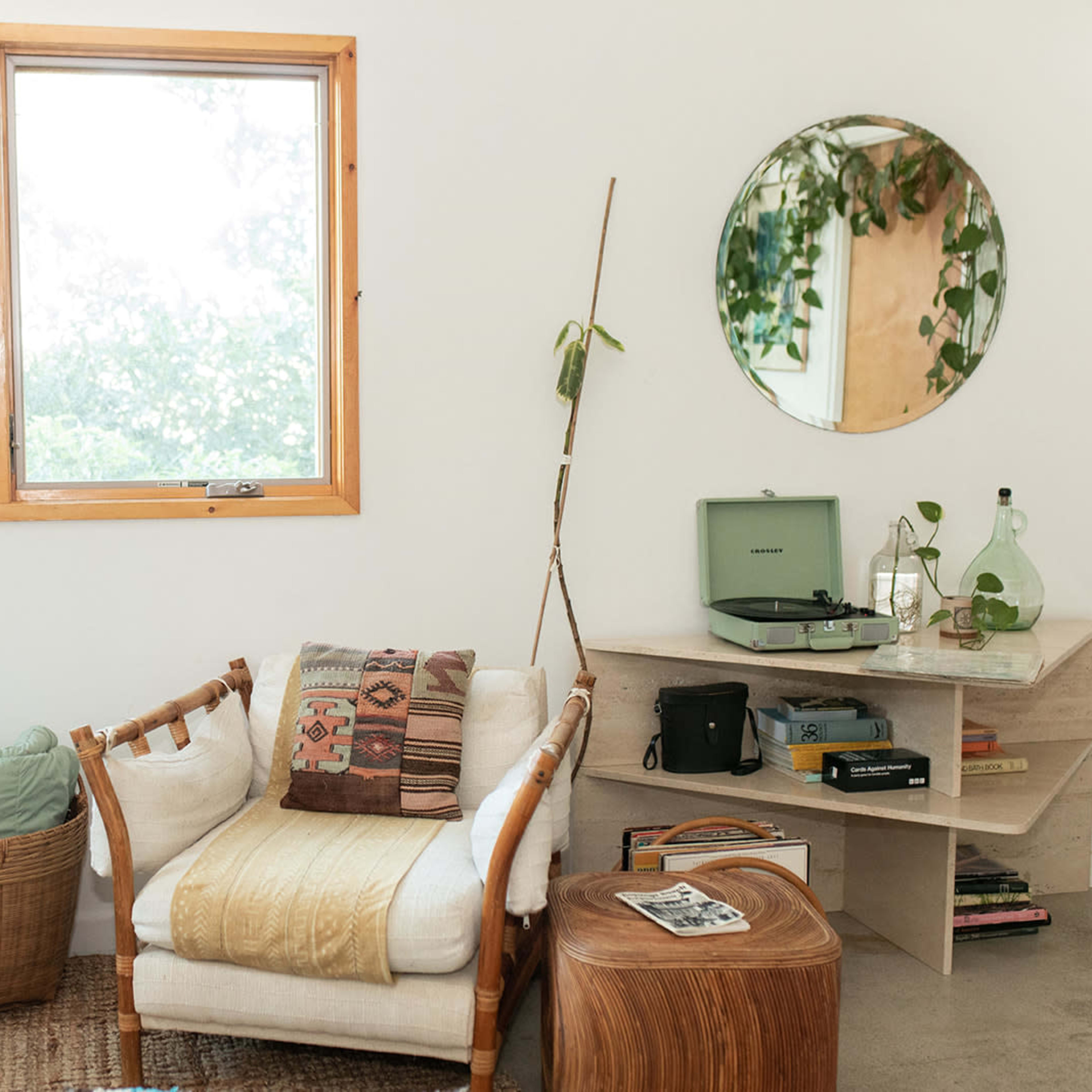 A cozy living space featuring a chair with a patterned throw, a small wooden side table, a record player on a shelf, and large windows that let in natural light.