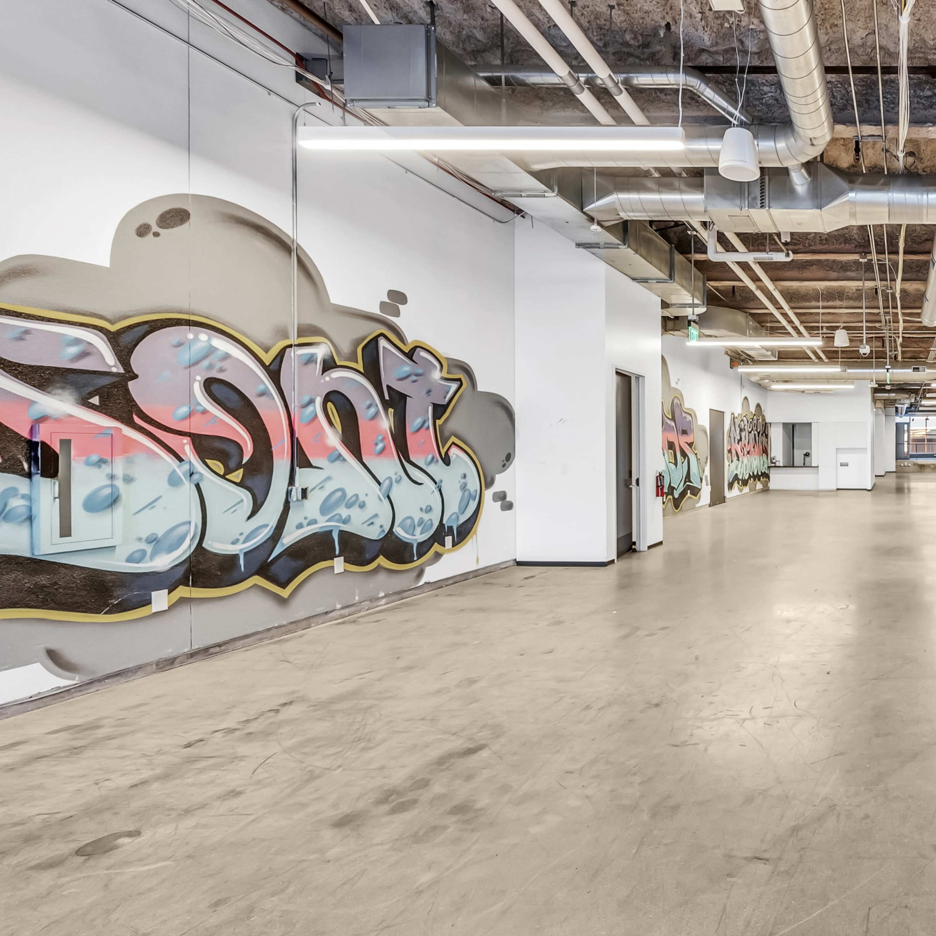 A spacious industrial corridor with graffiti-covered walls and exposed piping.