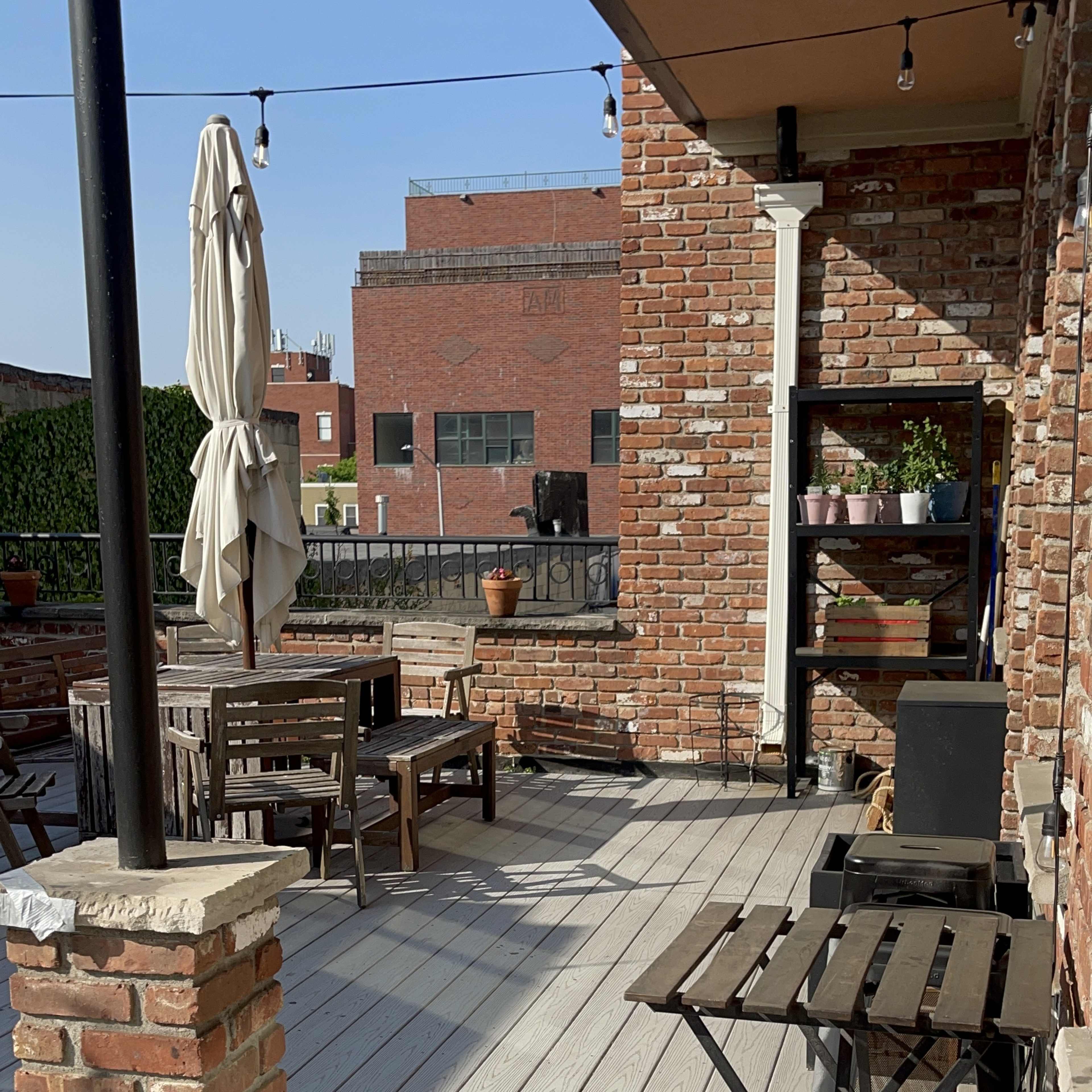 A wooden deck with brick walls and outdoor furniture, including a table and chairs, along with a potted plant and a large patio umbrella.