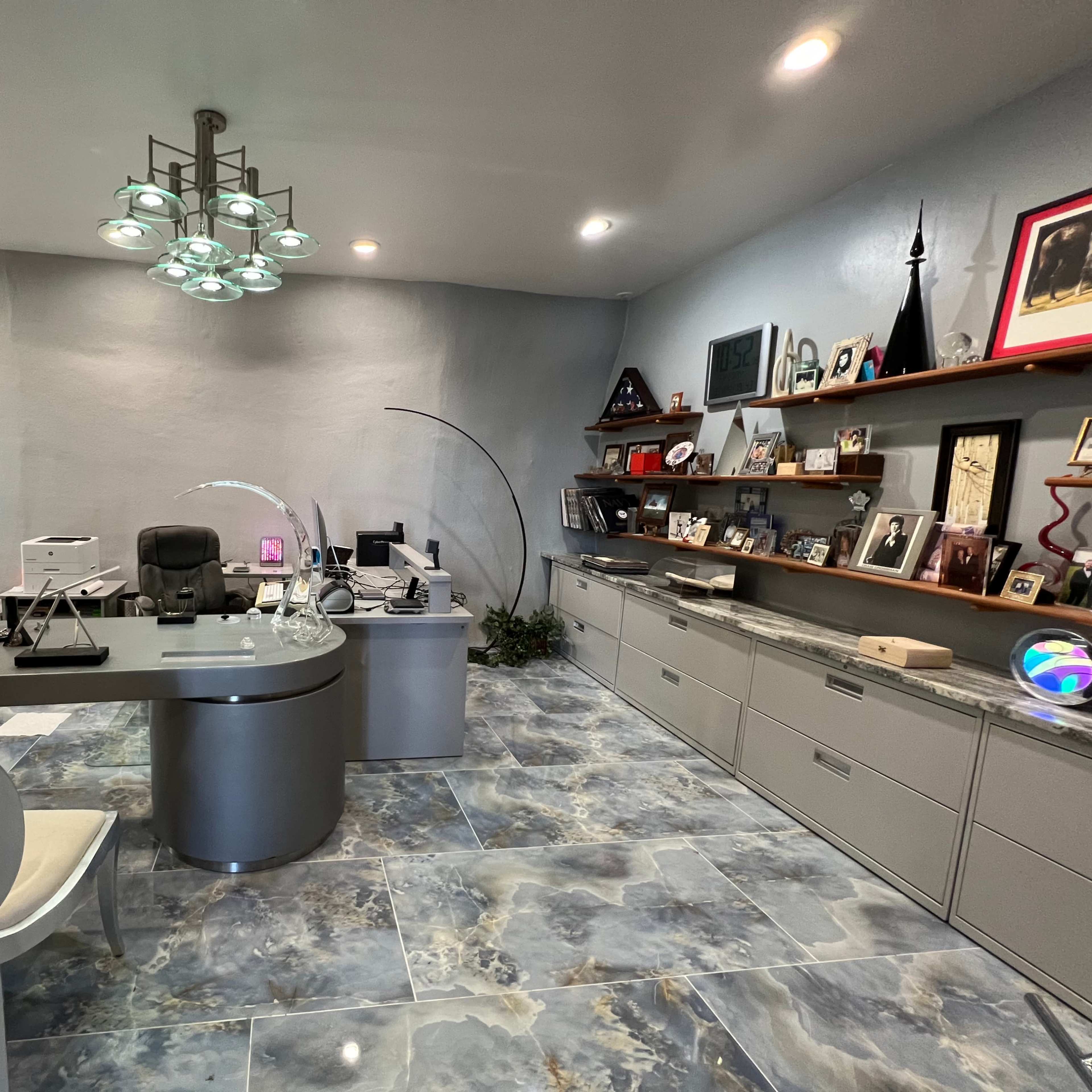 A modern office space featuring a sleek desk, a white chair, and shelves lined with photographs and decor items.