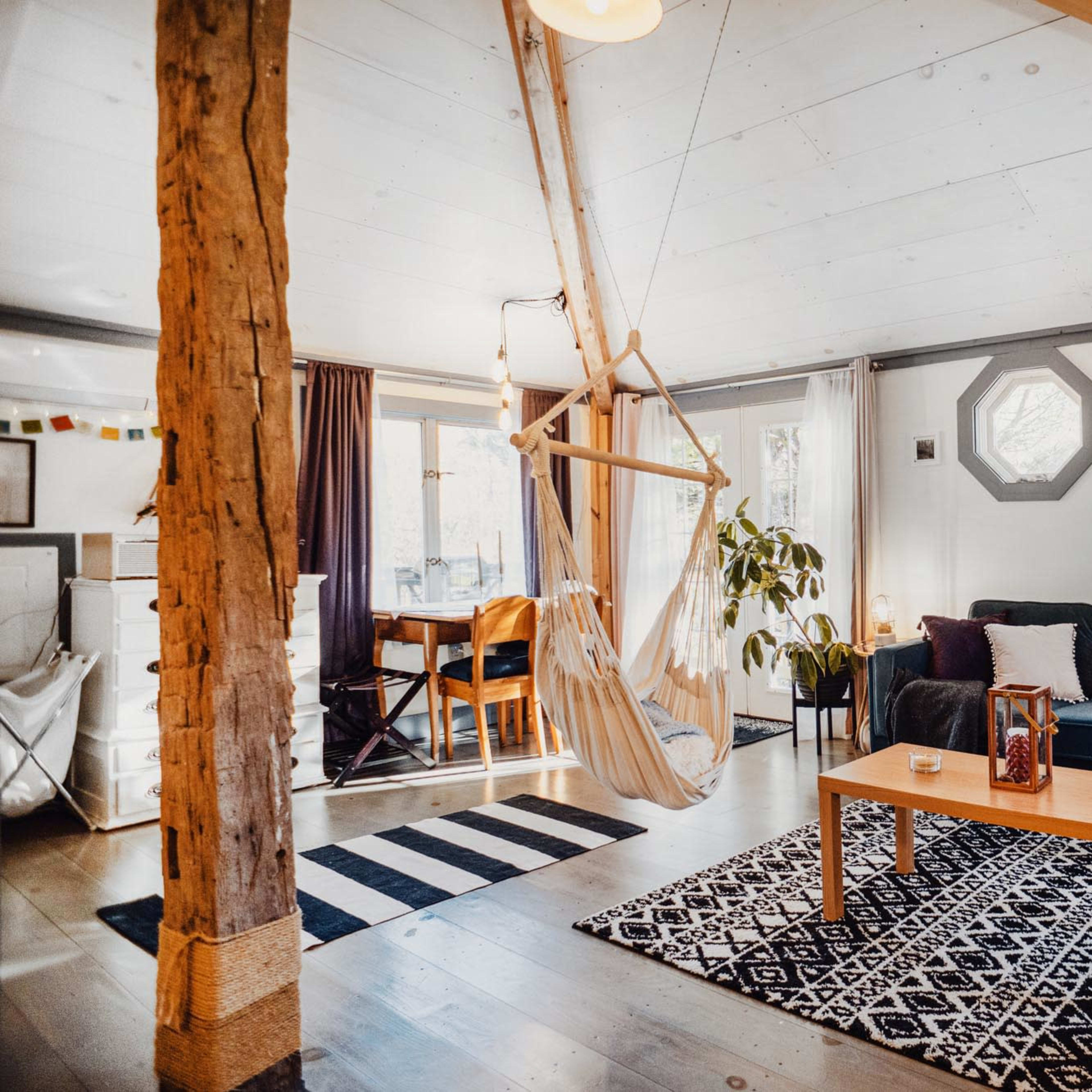 A modern living room with a hammock, a green sofa, a wooden coffee table, and a decorative rug on the floor.