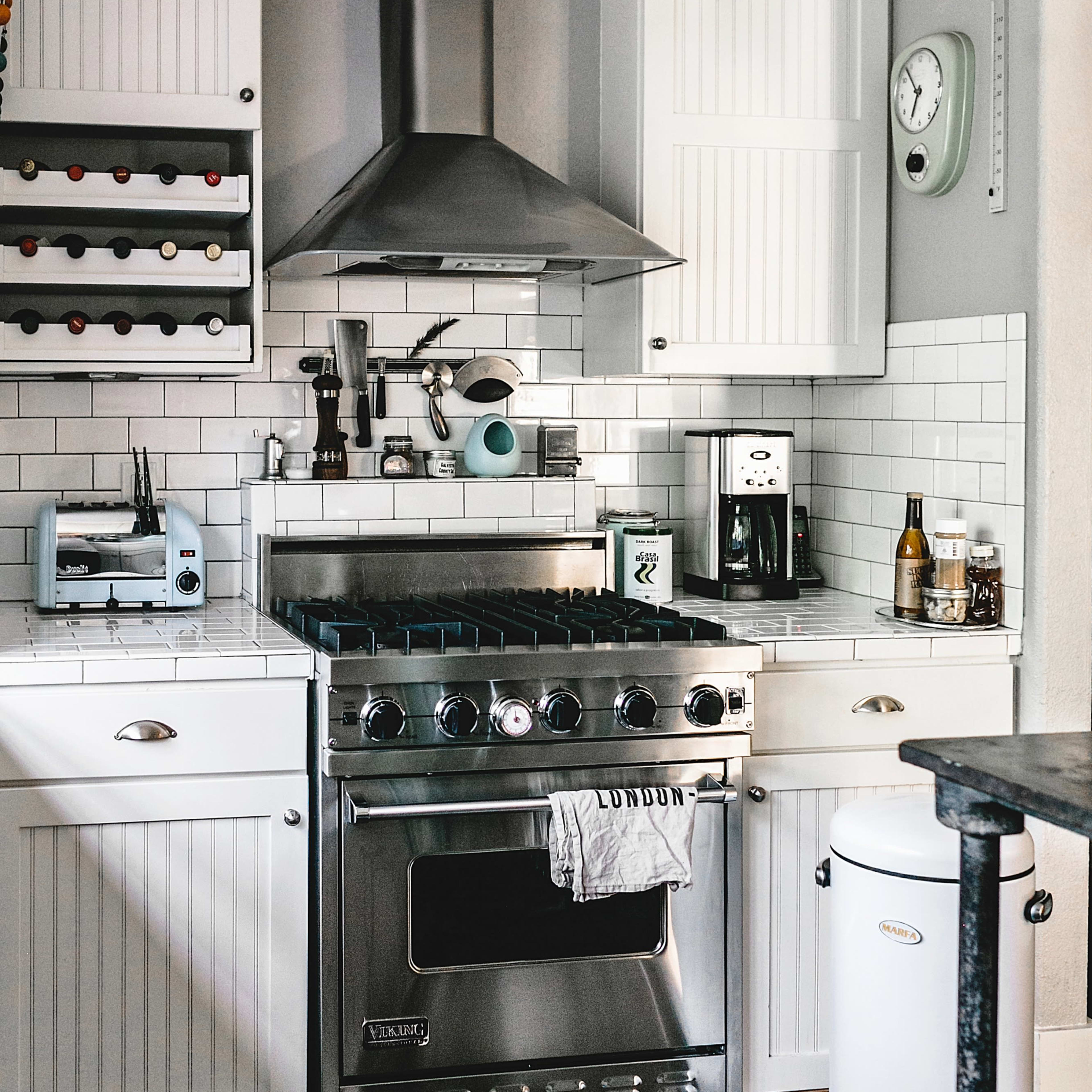 A modern kitchen featuring white cabinets, a stainless steel gas stove with an overhead hood, a coffee maker, and a wine rack.