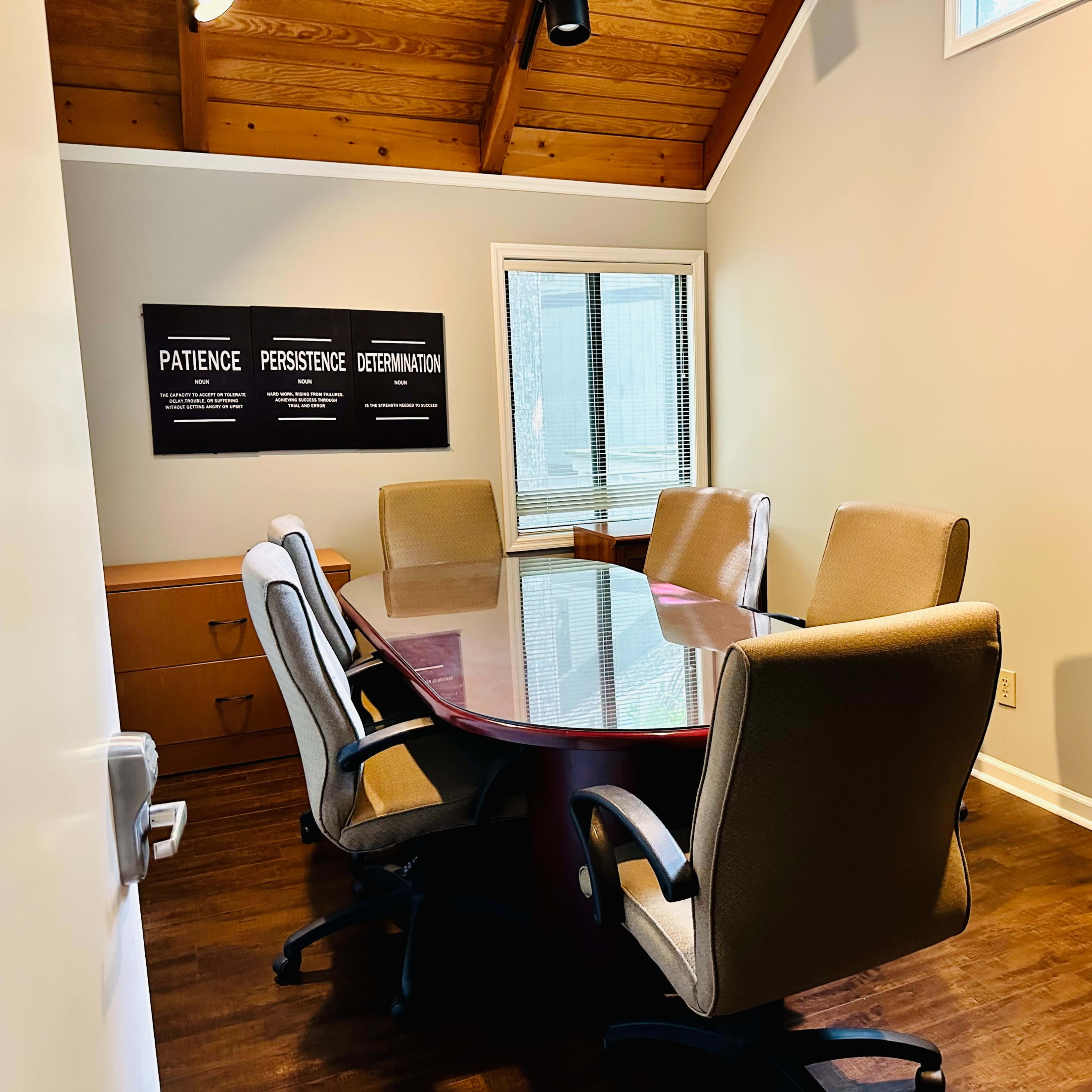 A conference room features a large oval table surrounded by six ergonomic chairs, with motivational posters on the wall.