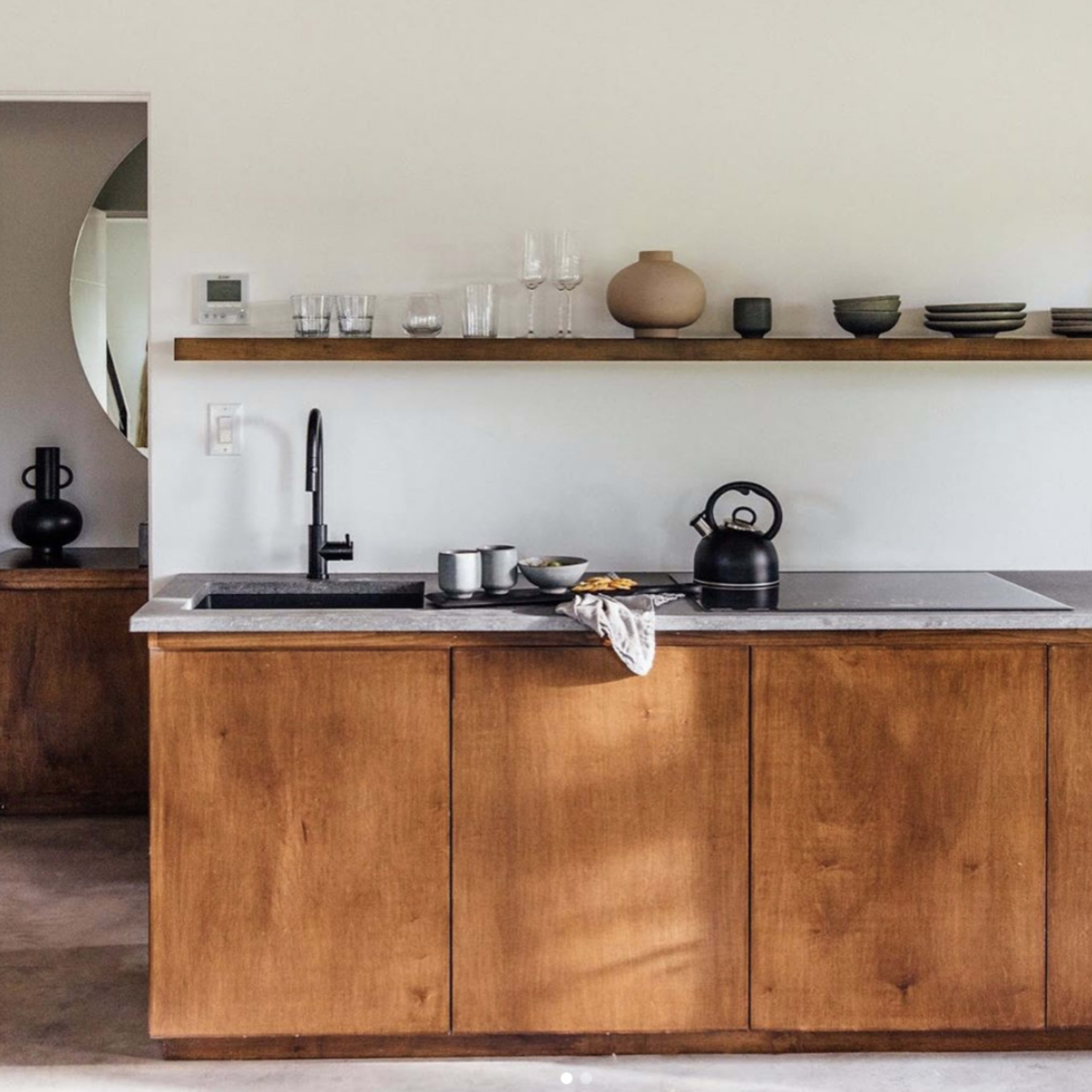 A modern kitchen with wooden cabinetry, a gray countertop, and minimalist decor on a floating shelf.
