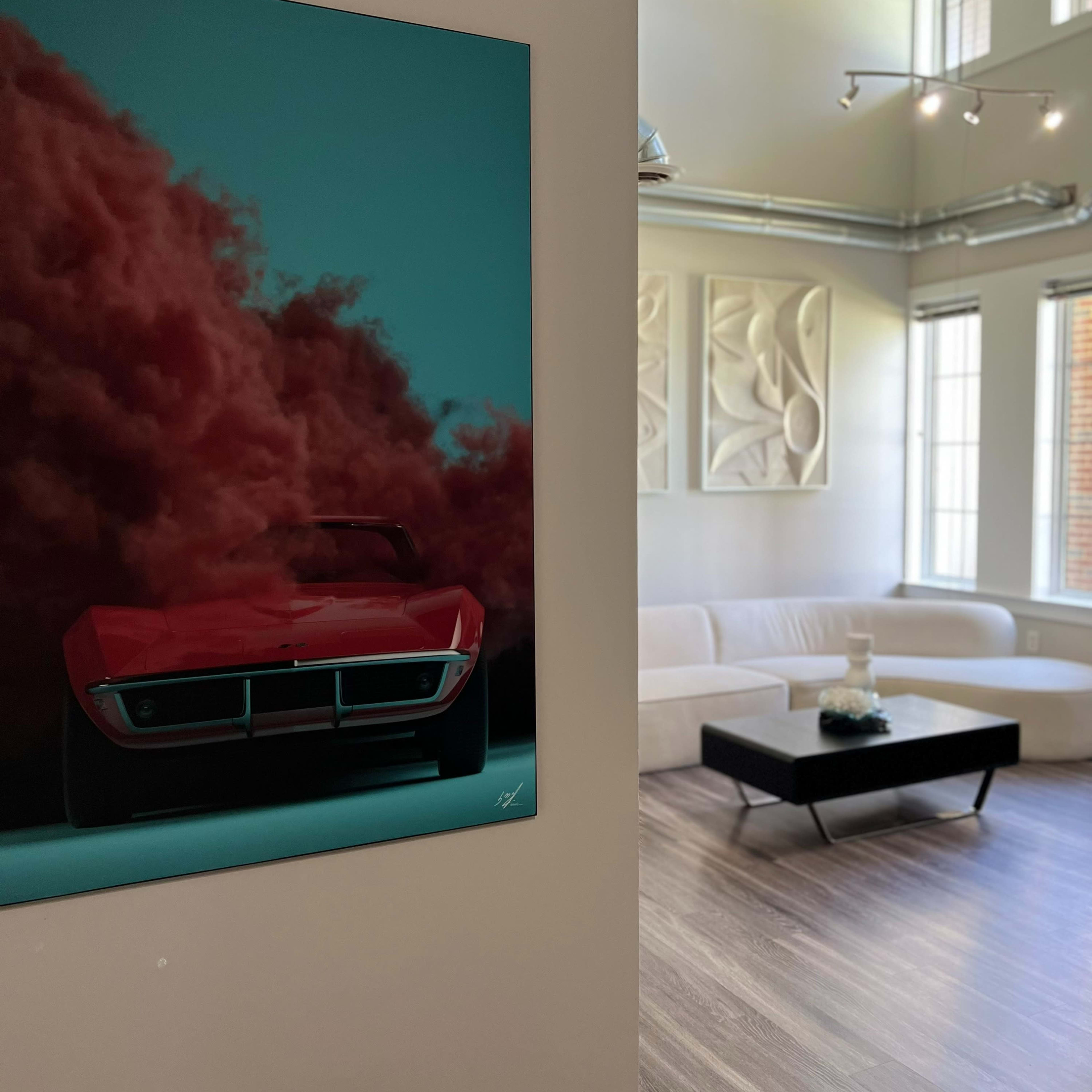 A red sports car painting hangs on a wall beside a modern living room with a white sofa and a black coffee table.