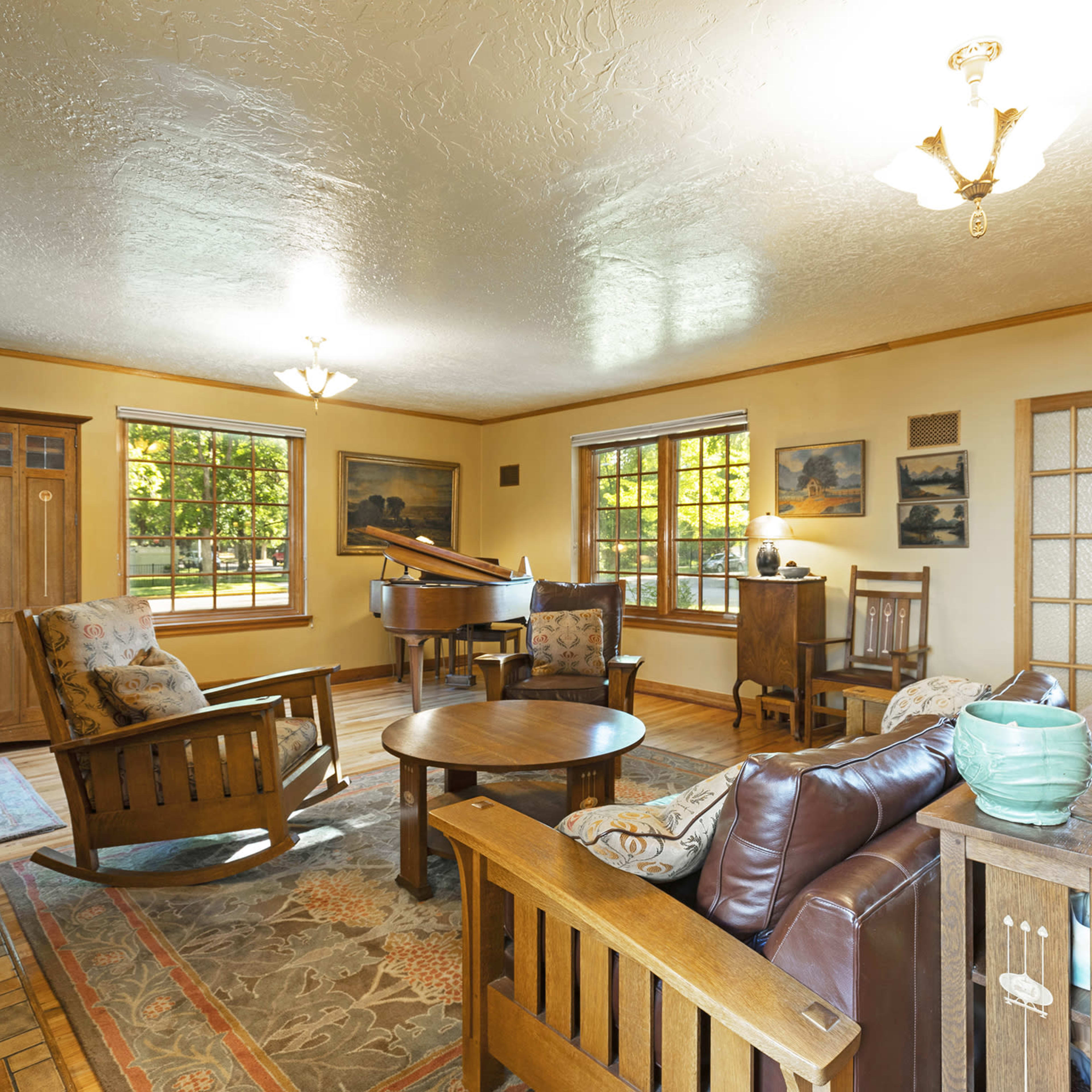 A cozy living room with wooden furniture, a circular table, and large windows allowing natural light.