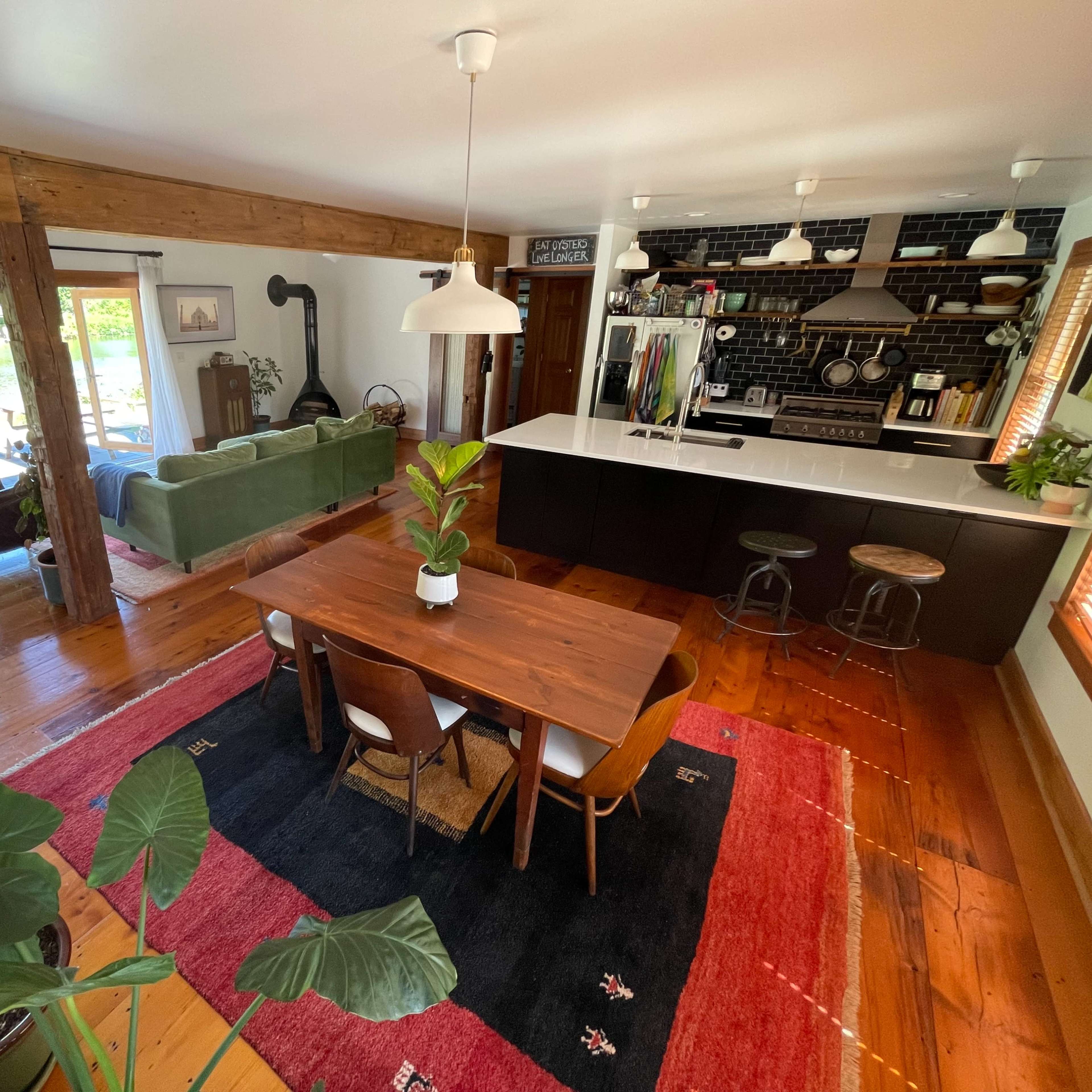 A modern open-concept living area with a dining table, kitchen, and large windows facing a body of water.