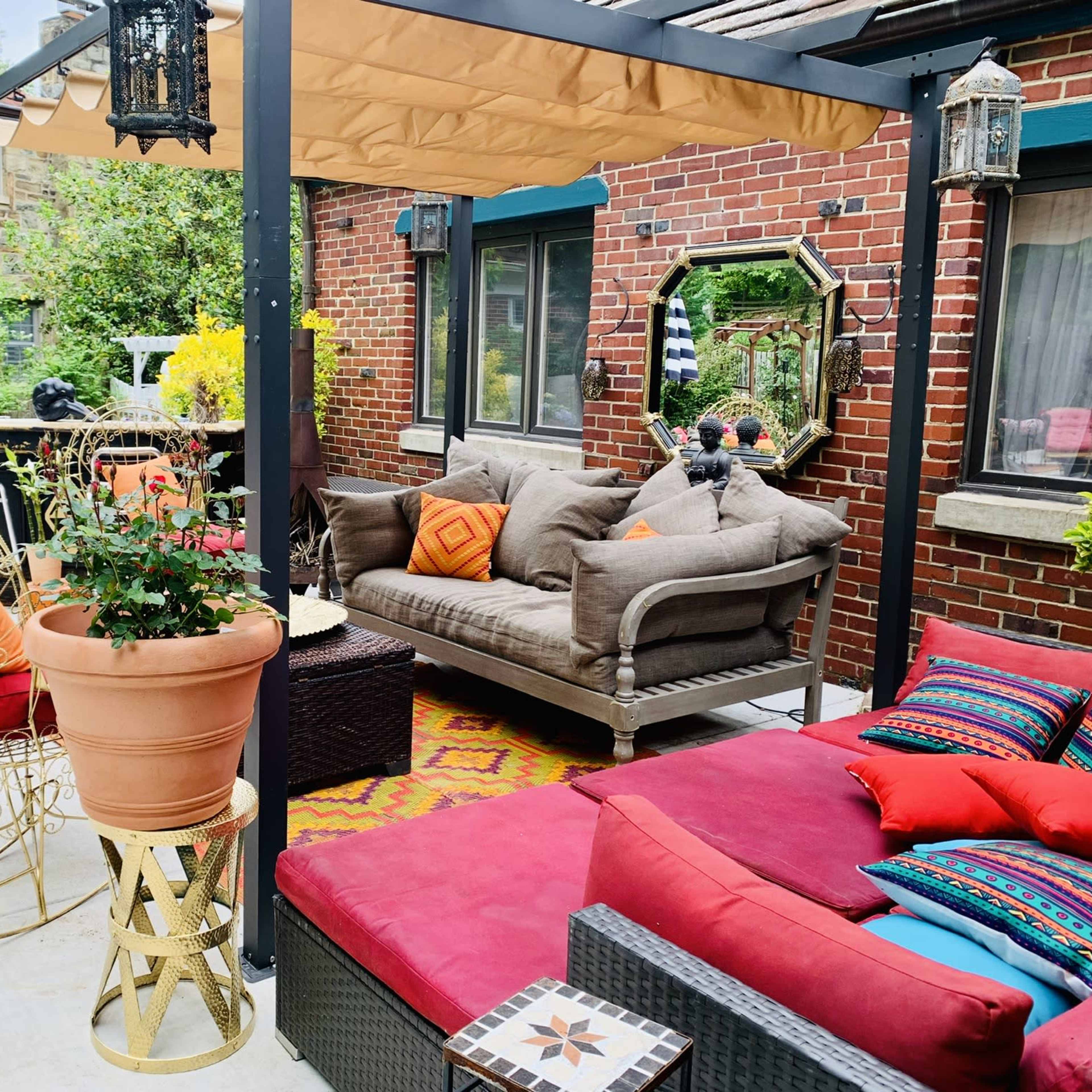 A patio area with a comfortable seating arrangement, colorful cushions, potted plants, and decorative lanterns under a canopy.