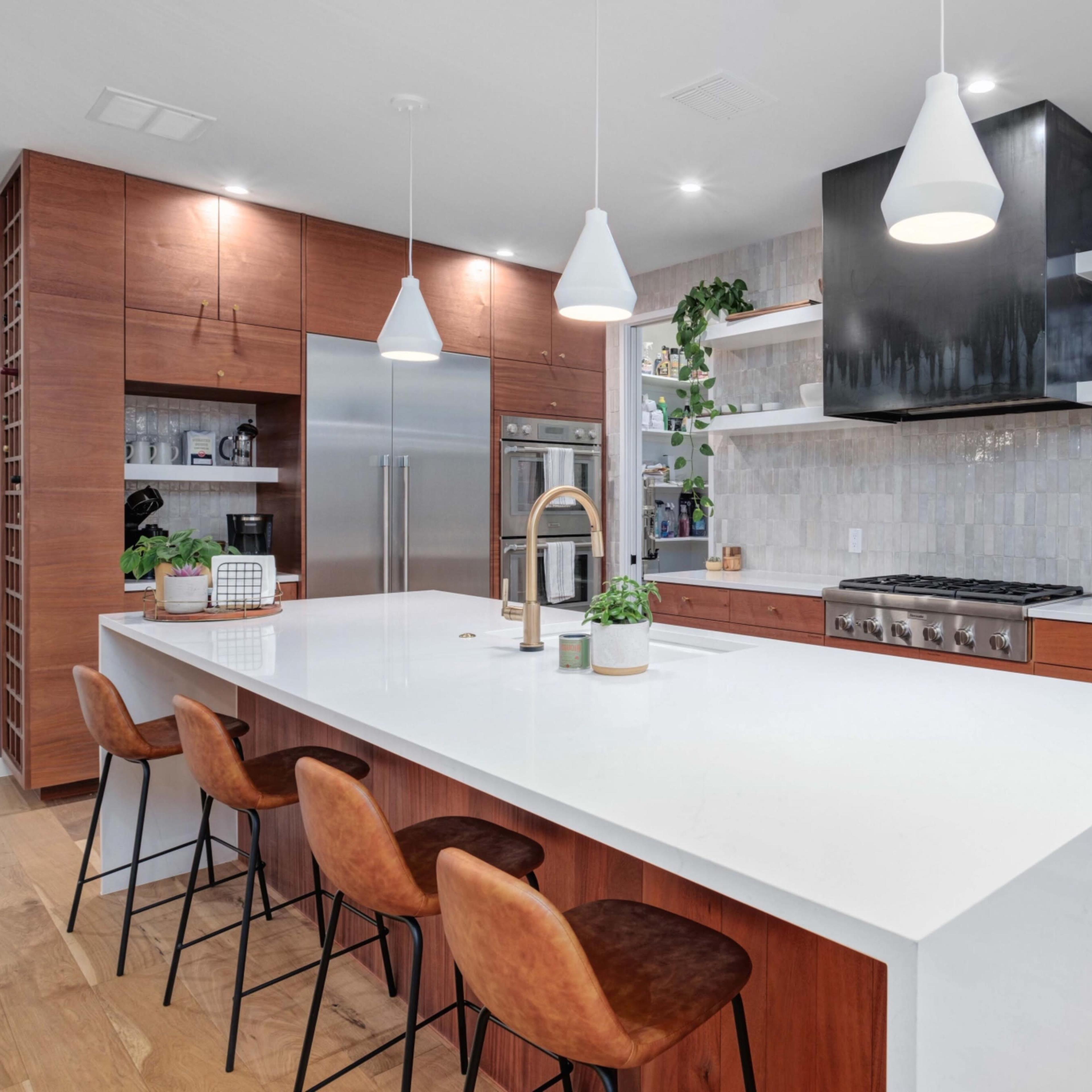 A modern kitchen features a large island with bar seating, stainless steel appliances, and wooden cabinetry.