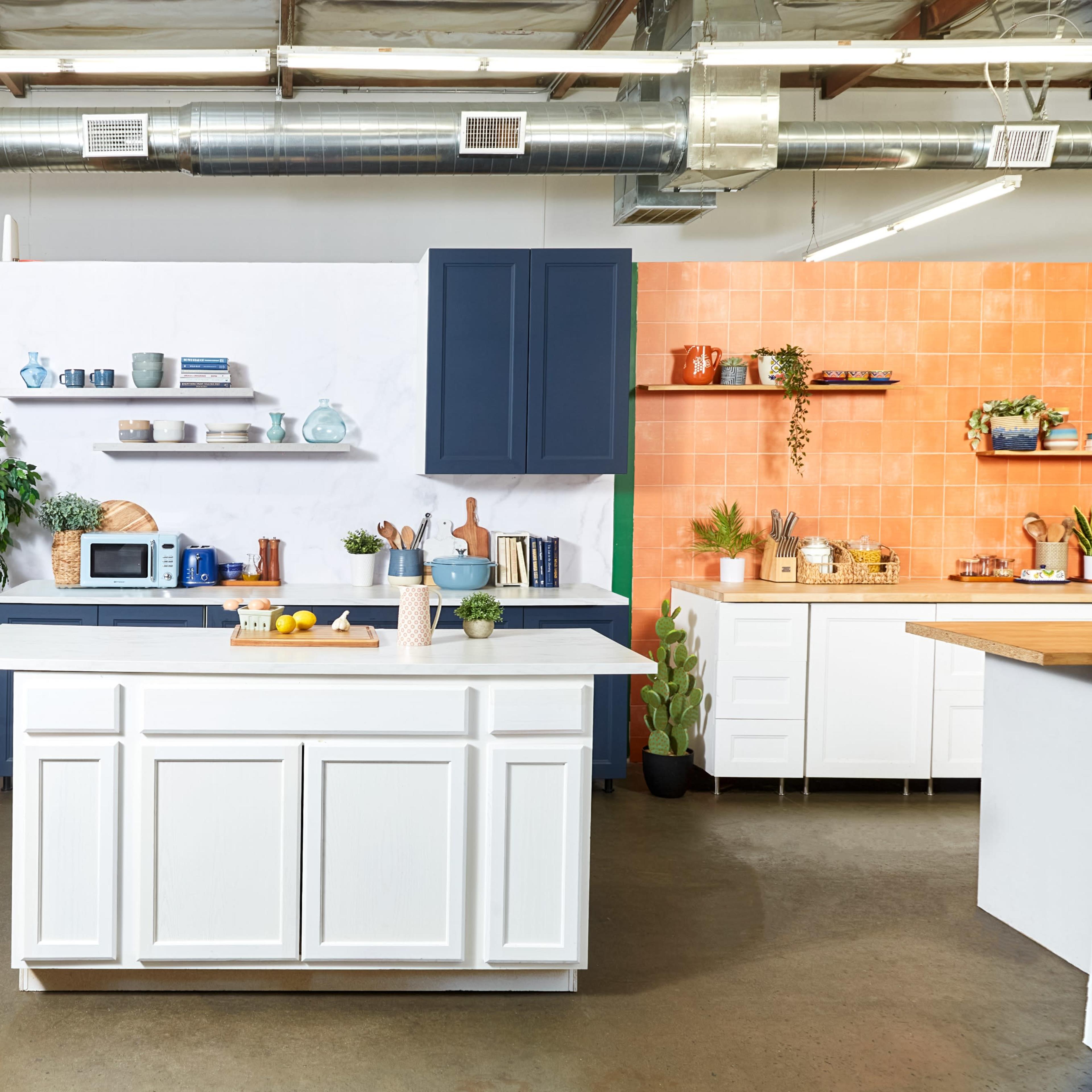 A modern kitchen space featuring a white island with a microwave, surrounded by various shelves and vibrant orange and blue accent walls.