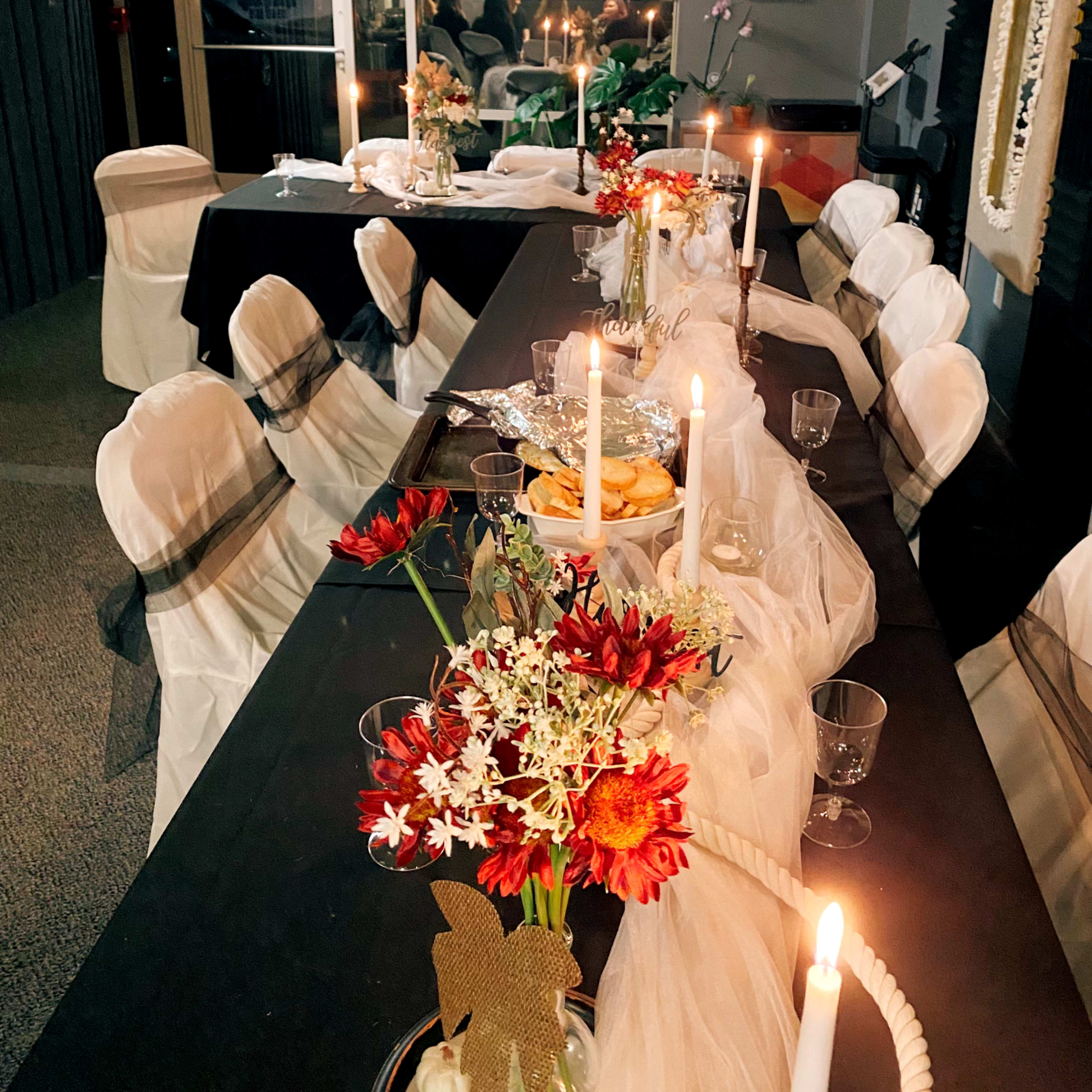 A long table is set for a formal gathering, decorated with flowers, candles, and tableware in a dimly lit room.