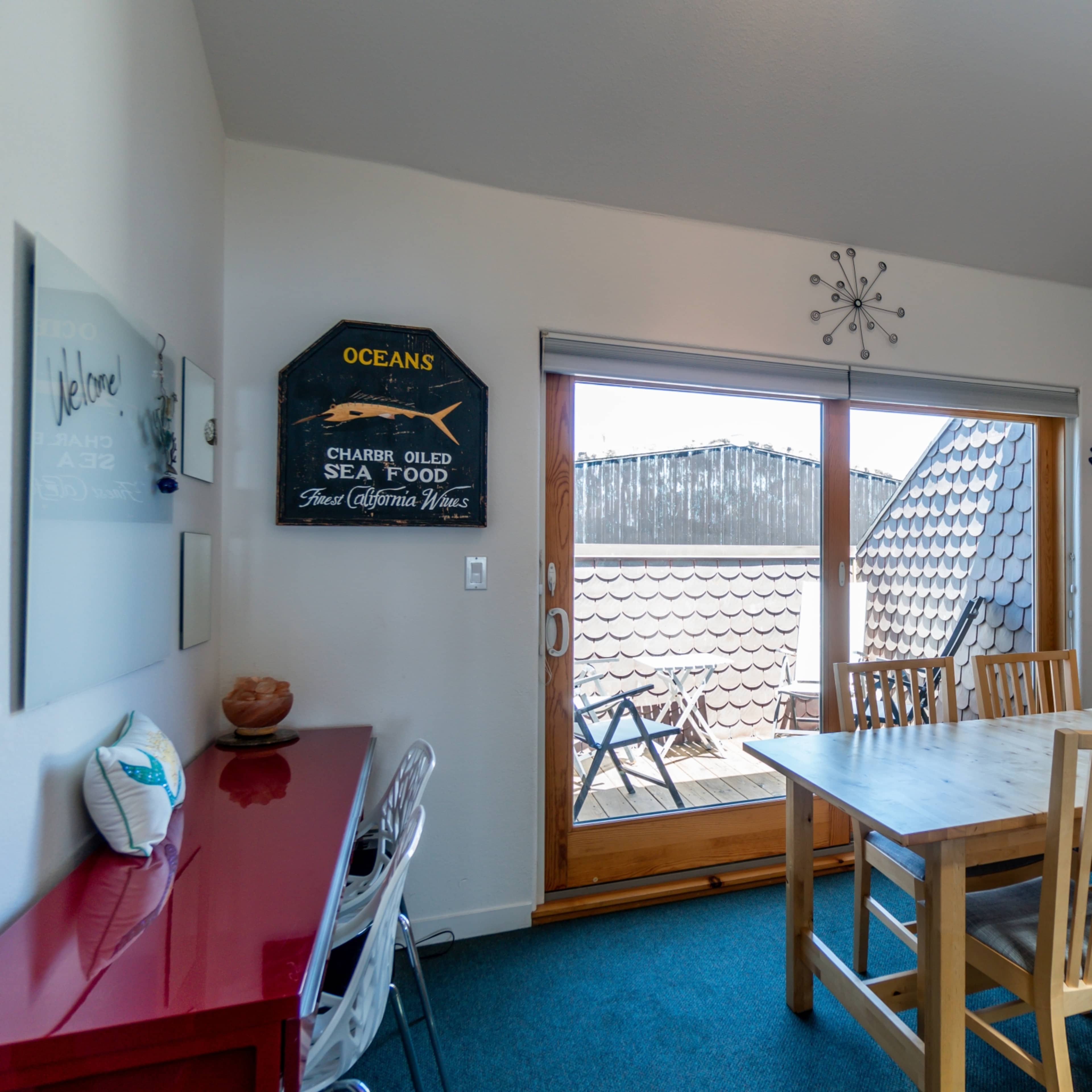 A dining area features a wooden table with four chairs, cabinets along the wall, and a large sliding door leading to an outdoor space.