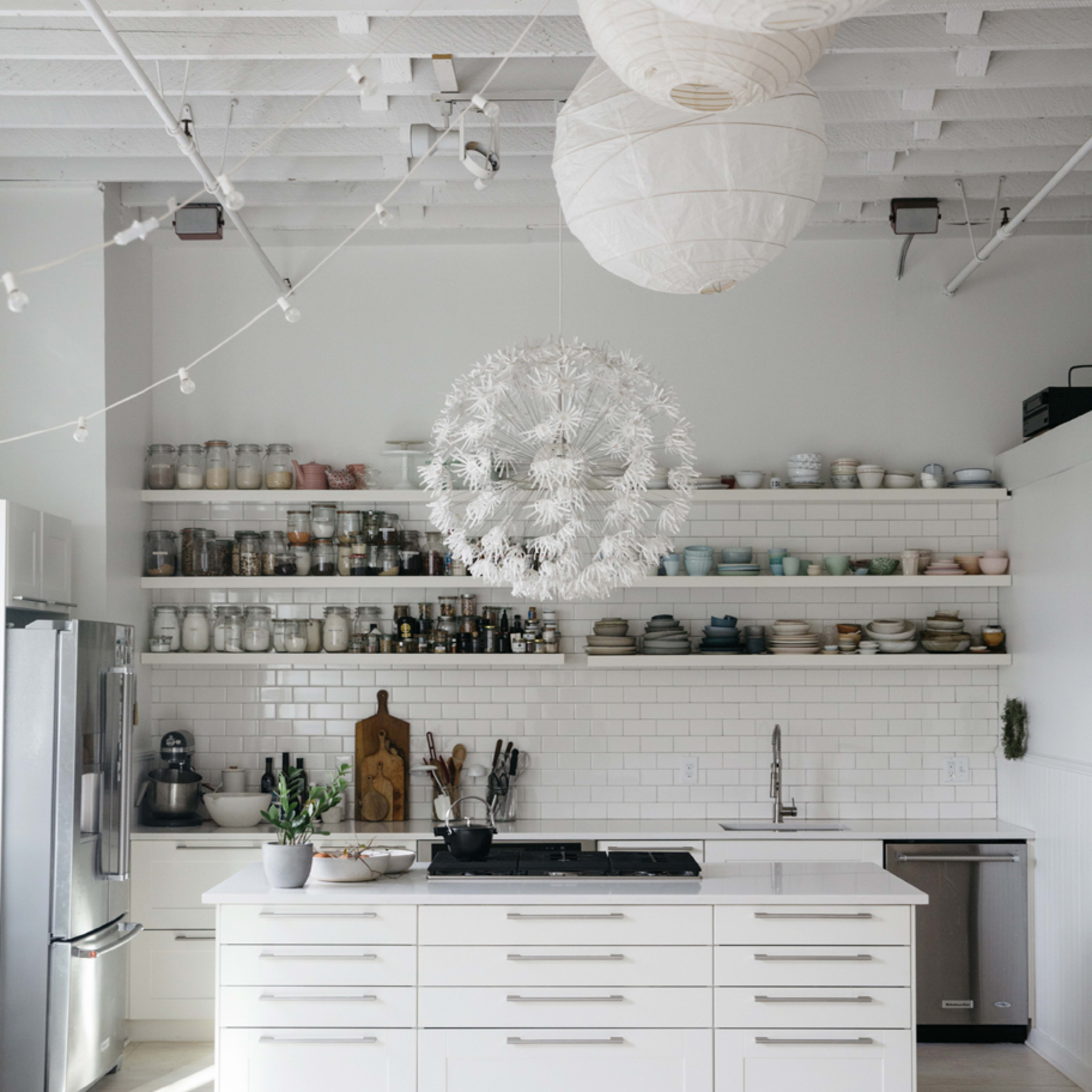 A modern kitchen features white cabinetry, open shelving with dishware, a central island with a cooktop, and pendant lighting.