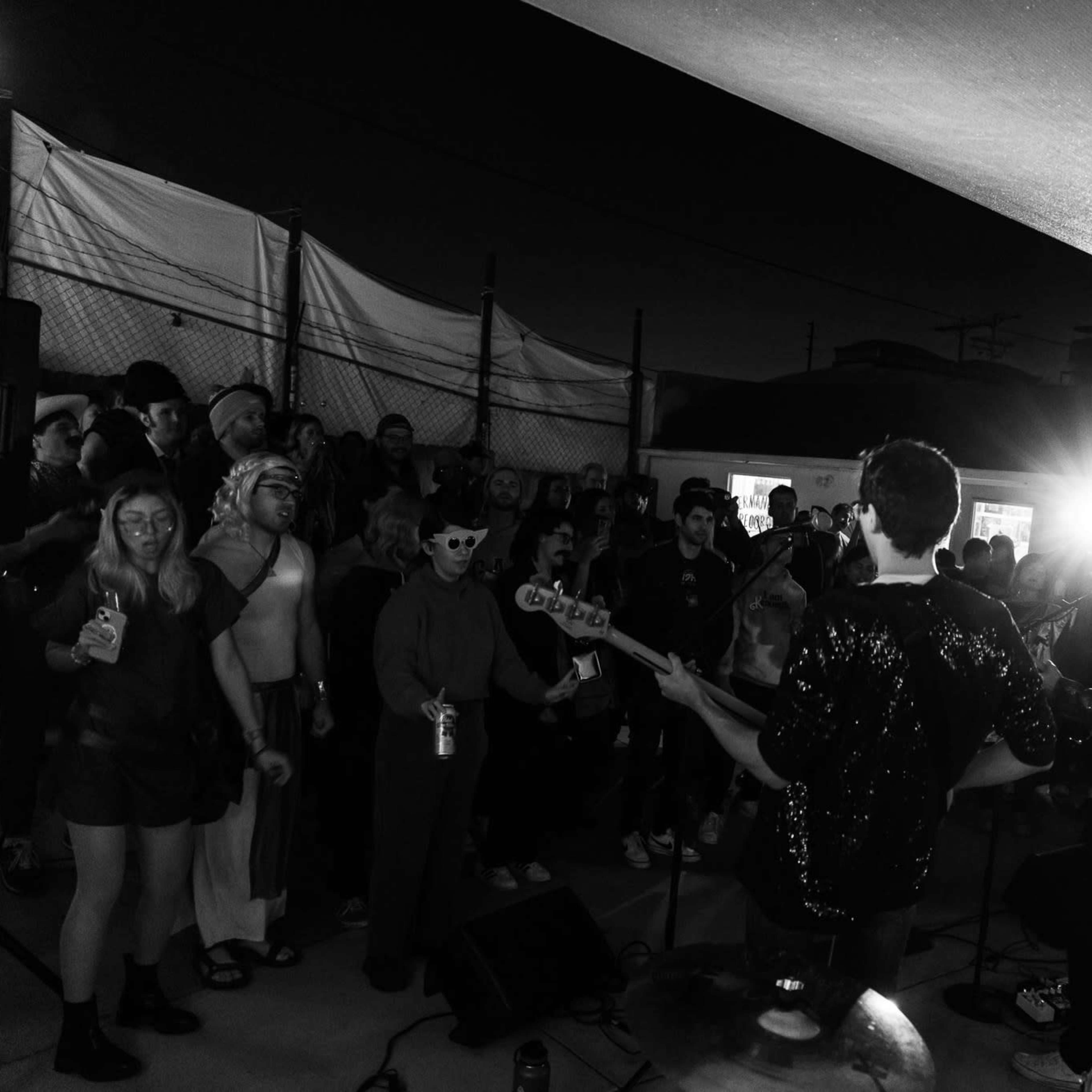 A band performs on stage while a crowd watches under dim lights at an outdoor venue.